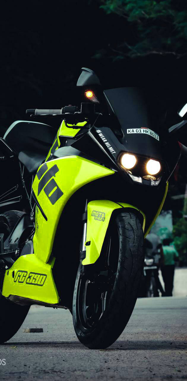 霓虹綠色KTM RC 200 壁紙 — 一輛霓虹黃色電單車，帶有發光頭燈，夜間停泊在黑暗的街道上，背景有樹木。