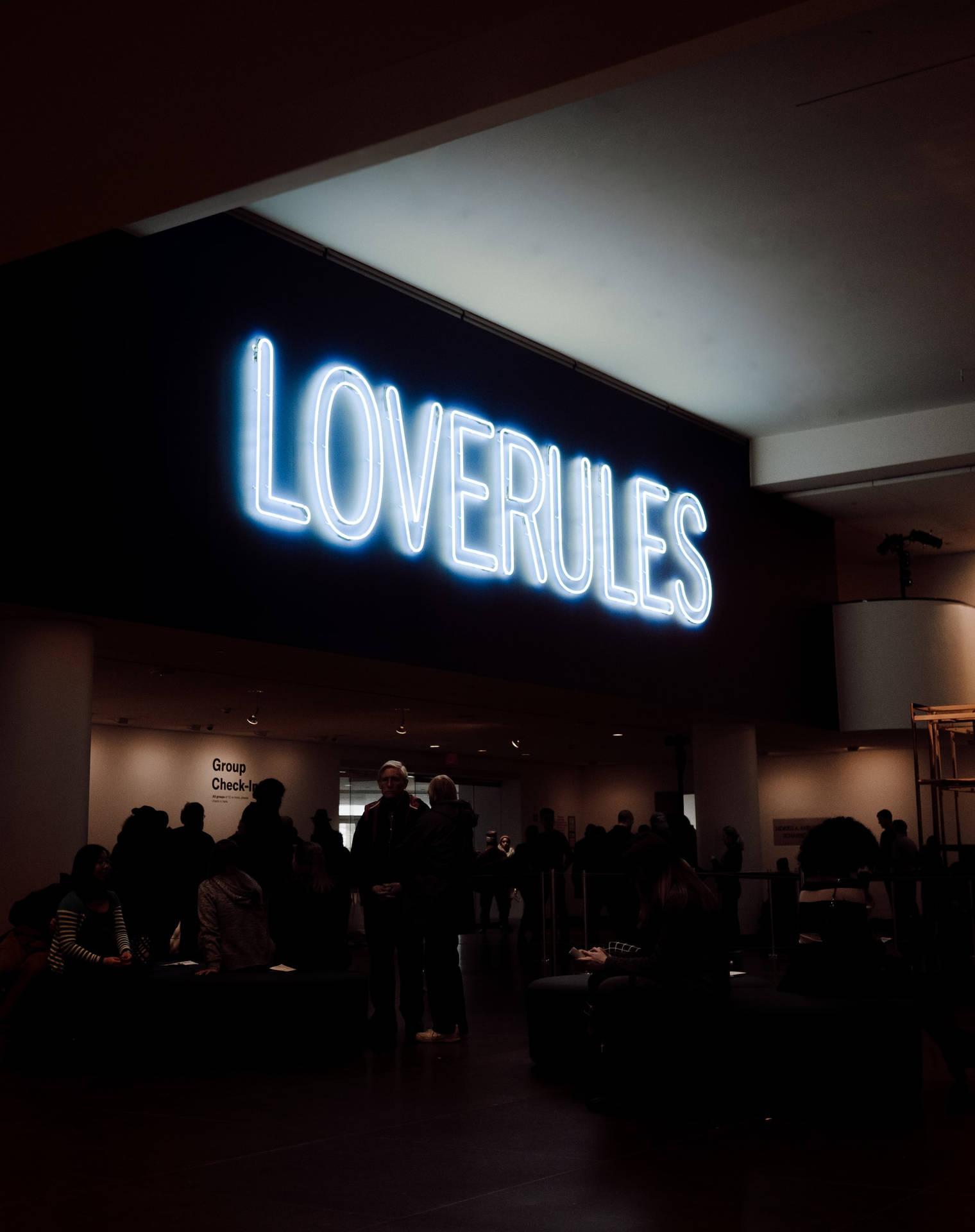 一個明亮的藍色霓虹燈牌寫著LOVERULES，在一個黑暗的房間裡，有人。
