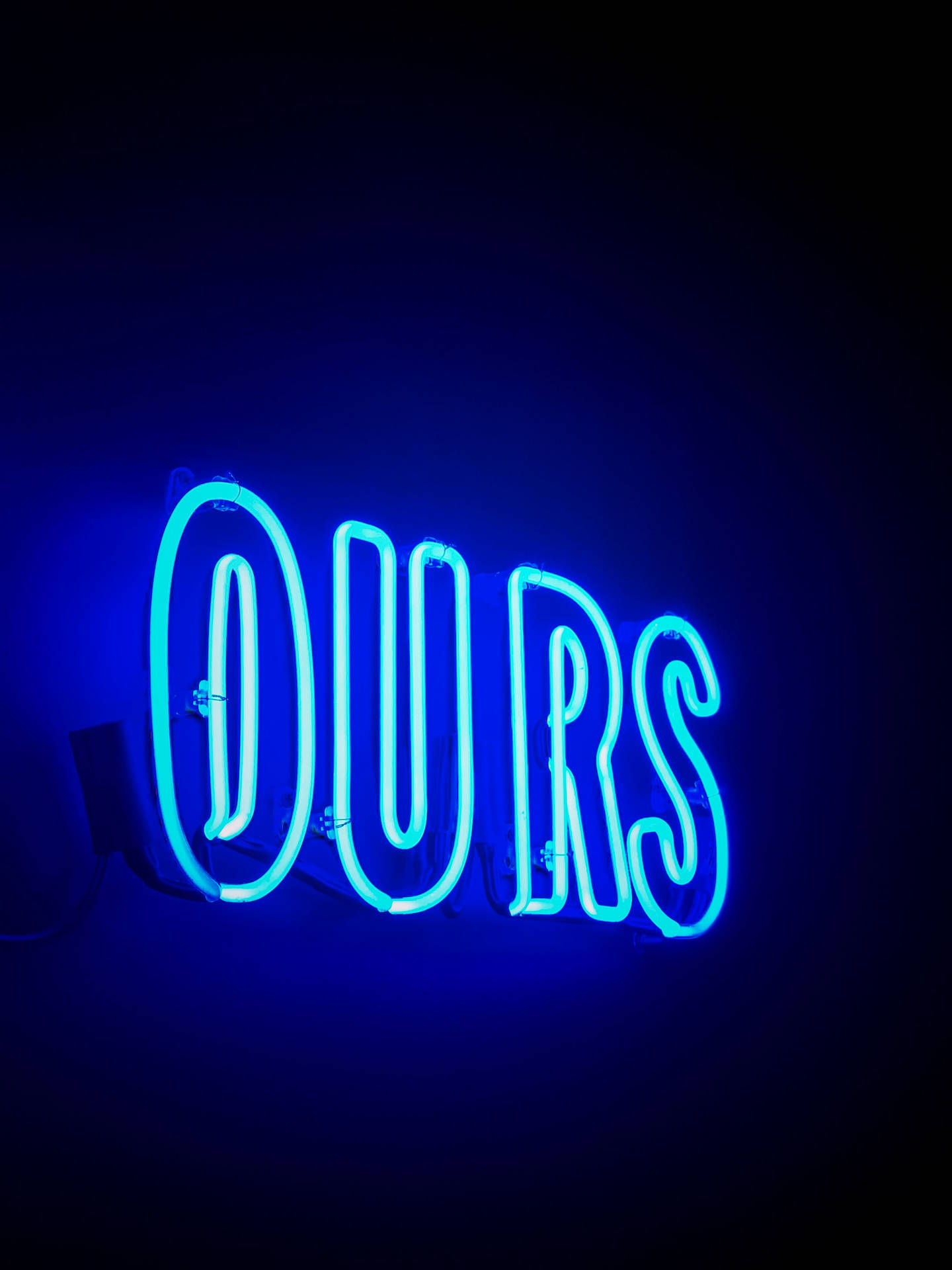 霓虹藍色「Ours」字樣 壁紙 — 一個發光的藍色霓虹燈牌，拼寫著「OURS」，在極簡環境中對著深色牆壁投射出鮮豔的光芒。
