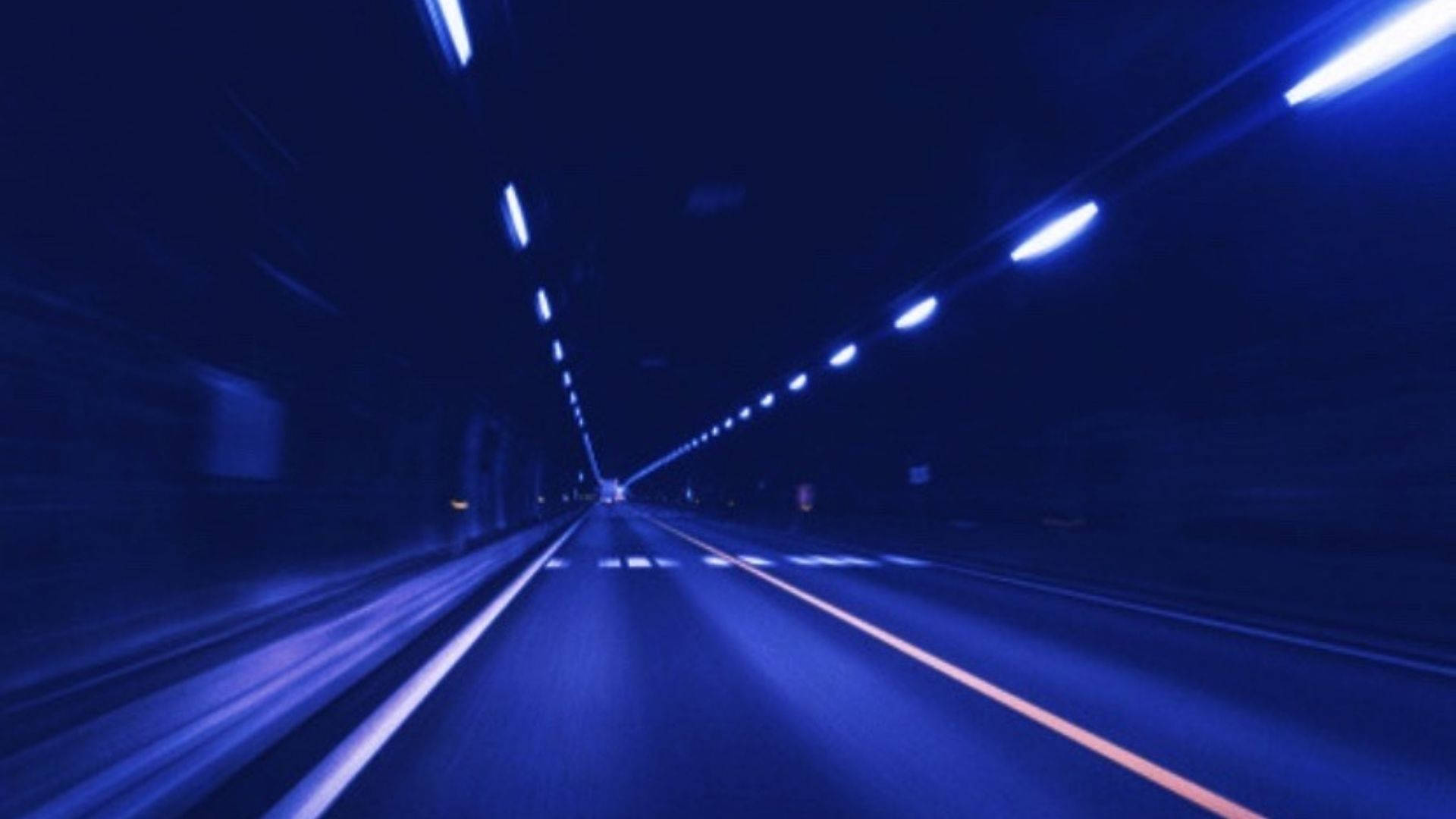 高速夜間駕駛時，藍色隧道燈光的條紋模糊掠過。