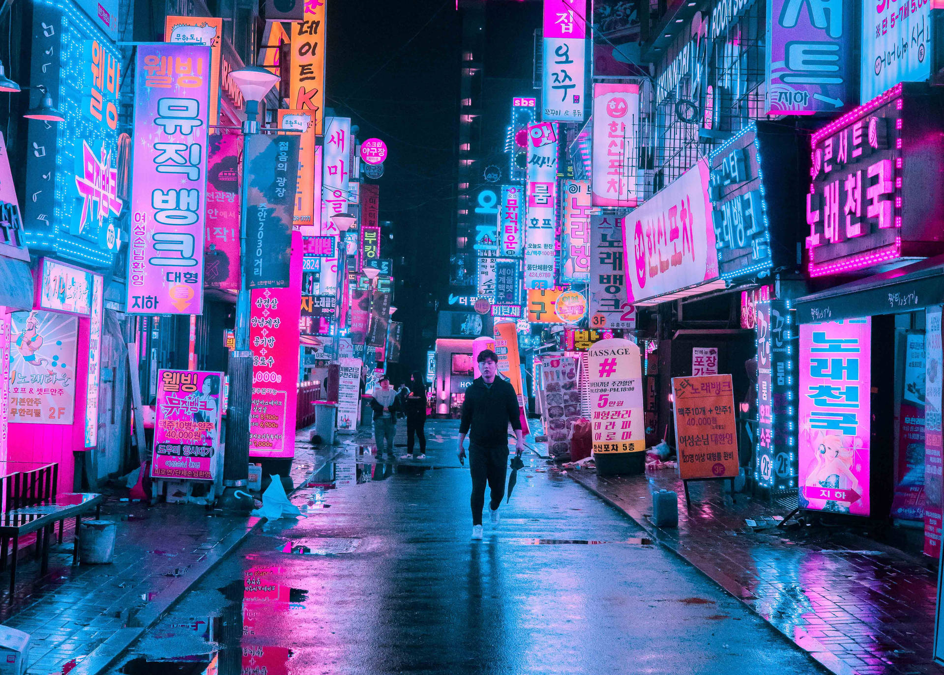 一個人在夜晚走過霓虹燈照亮的韓國街道，潮濕路面有倒影。