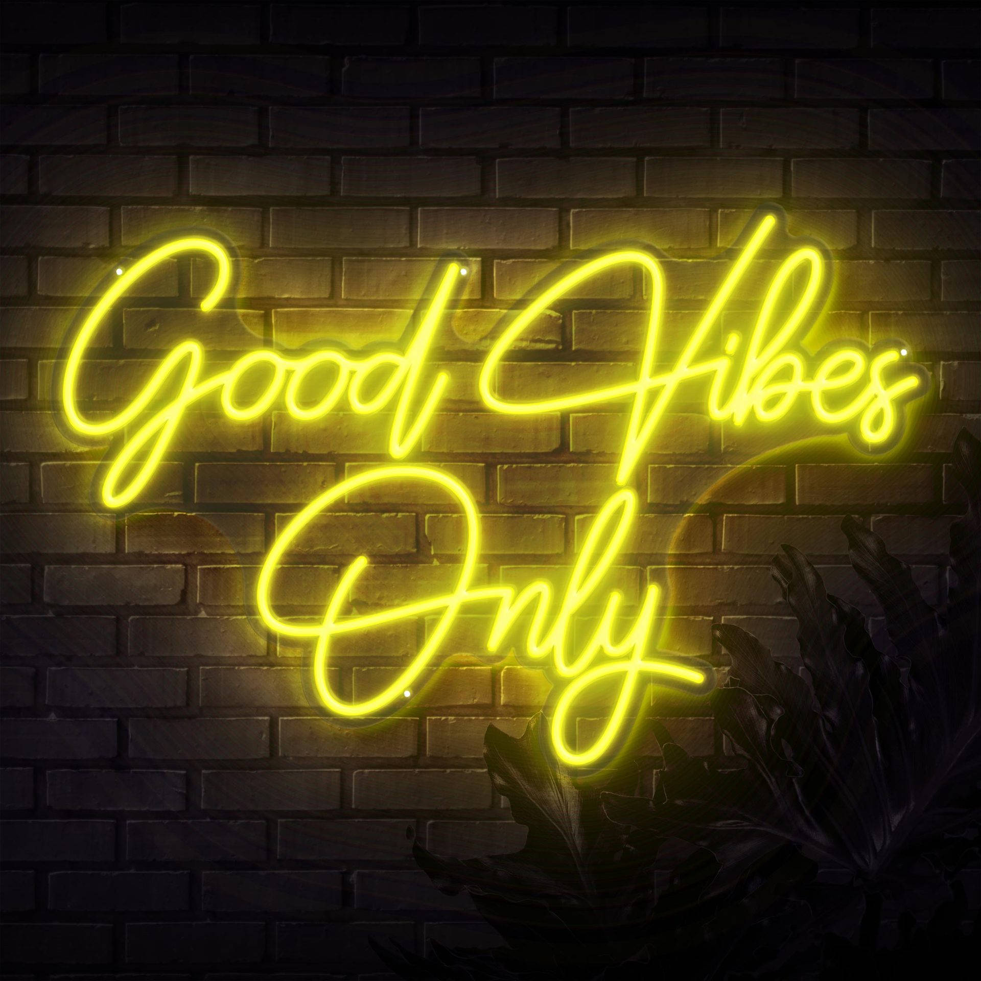 霓虹黃色「Good Vibes Only」文字 壁紙 — 一個發光的黃色霓虹燈牌，上面寫著「Good Vibes Only」，照亮了下方有茂密葉子的深色磚牆。