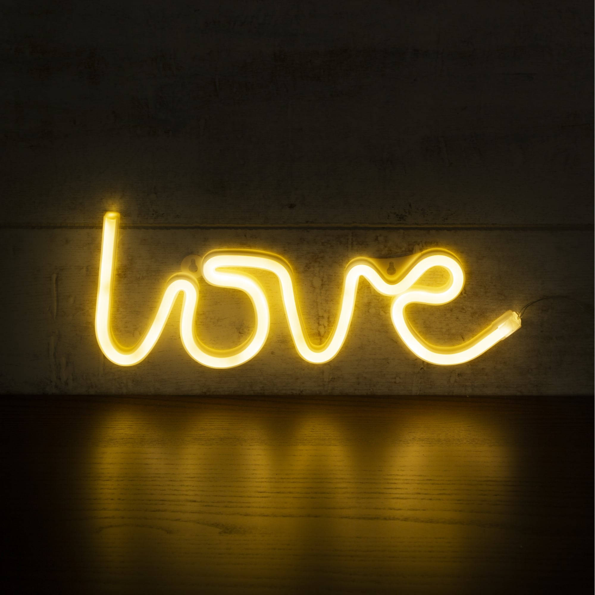 霓虹黃色「愛」字 壁紙 — 一個發光的黃色霓虹燈牌拼出love，在深色紋理牆壁的背景下，在木地板上投射出溫暖的倒影。
