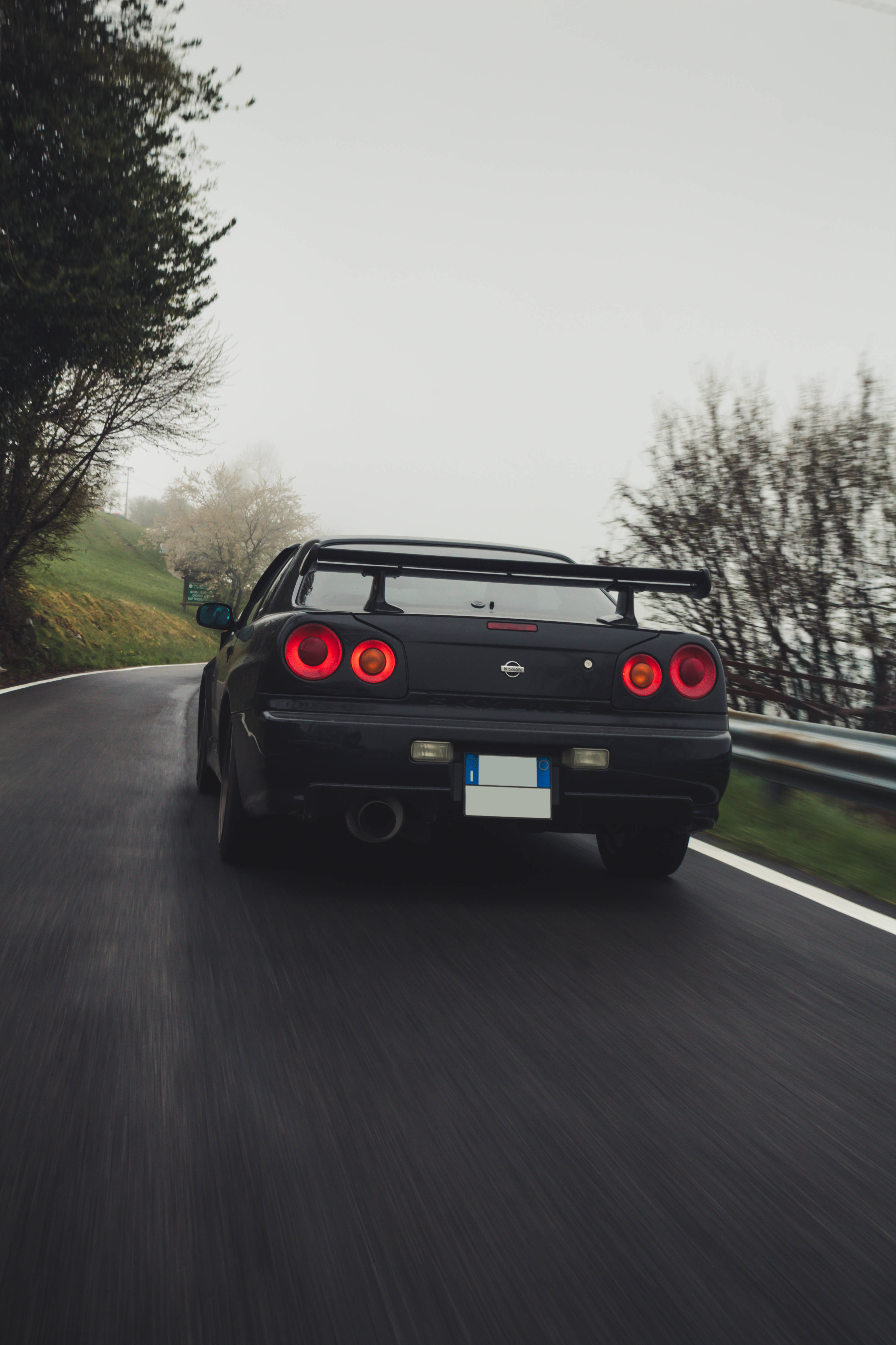 霧中 Nissan Skyline GTR R34 壁紙 — 一輛黑色日產R34 GT-R在霧氣瀰漫的山路上疾馳，紅色尾燈閃爍，動作模糊。