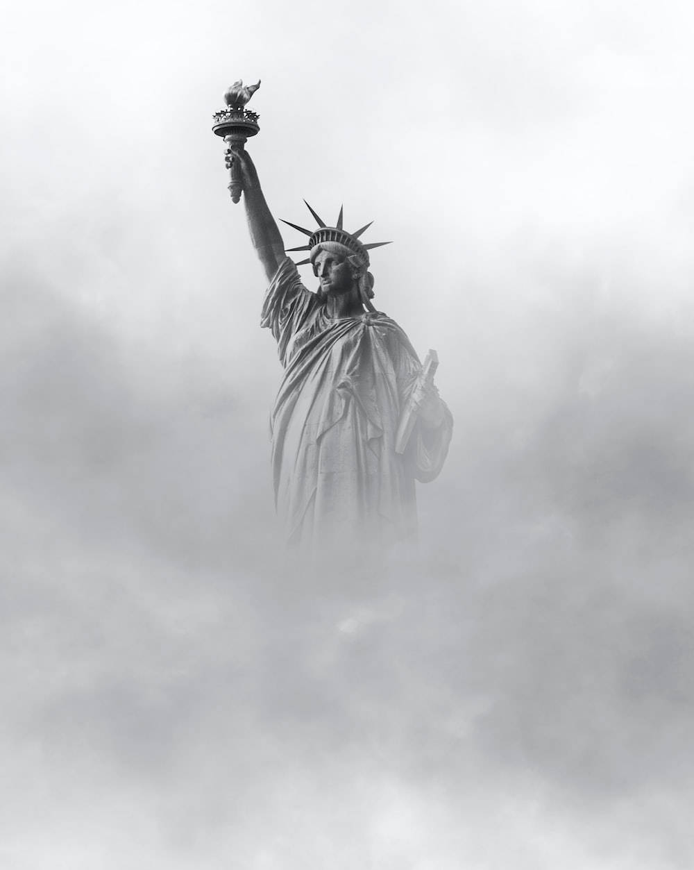 自由女神像穿過厚厚的灰色雲層升起，營造出憂鬱的黑白照片氛圍。