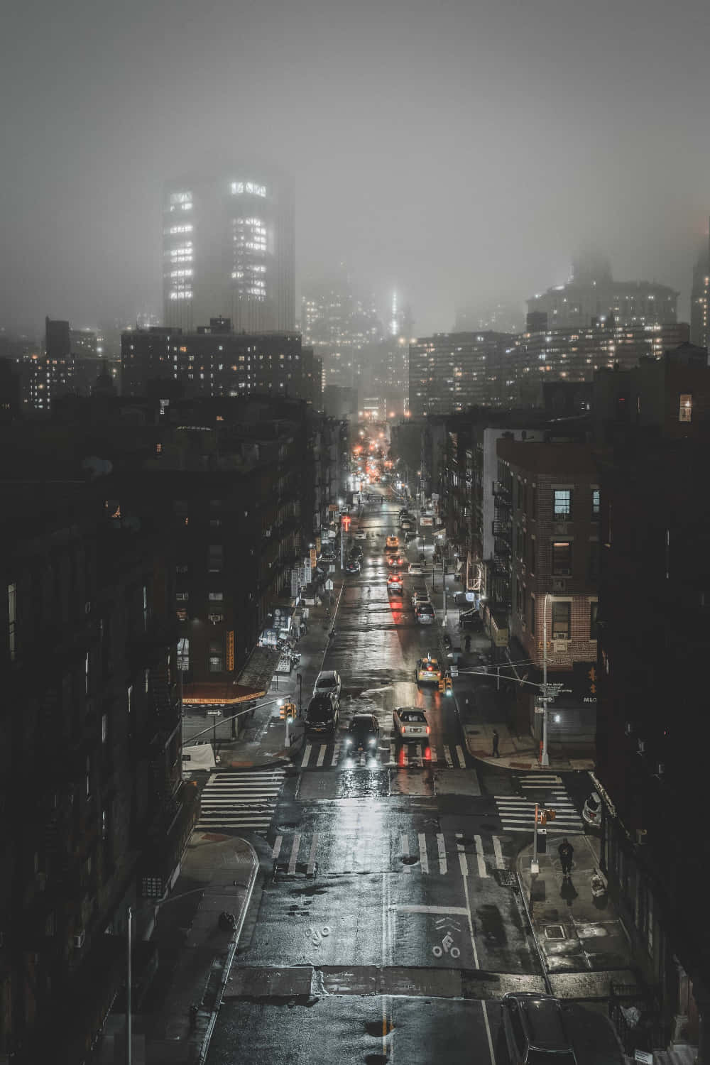 夜晚一條潮濕的城市街道，閃爍的車燈和遠處霧濛濛的摩天大樓。
