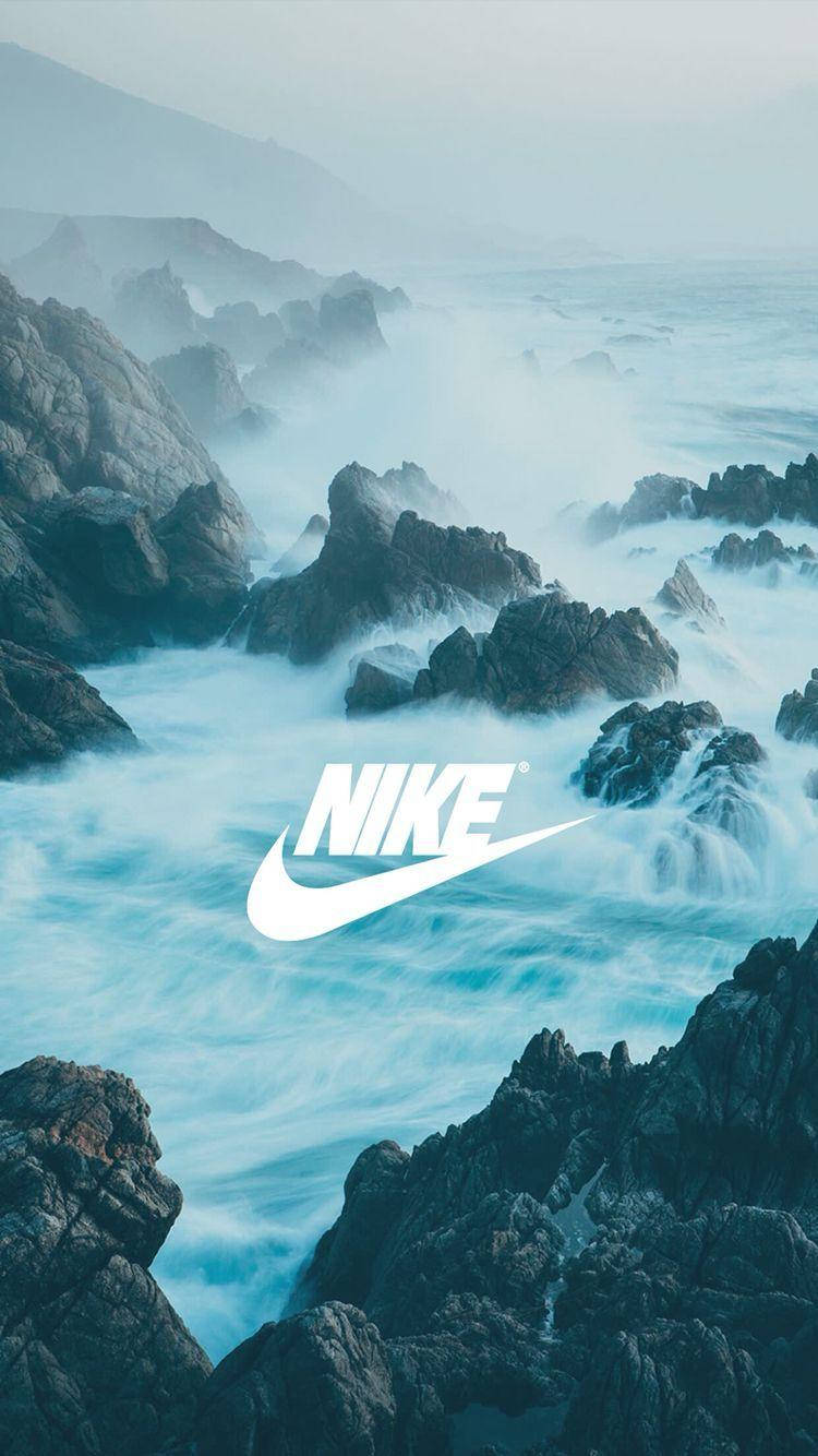 霧氣岩石懸崖耐克 iPhone 背景 壁紙 — 強勁的海浪拍打著堅固的海岸岩石，天空迷濛，中央有一個醒目的白色Nike標誌。