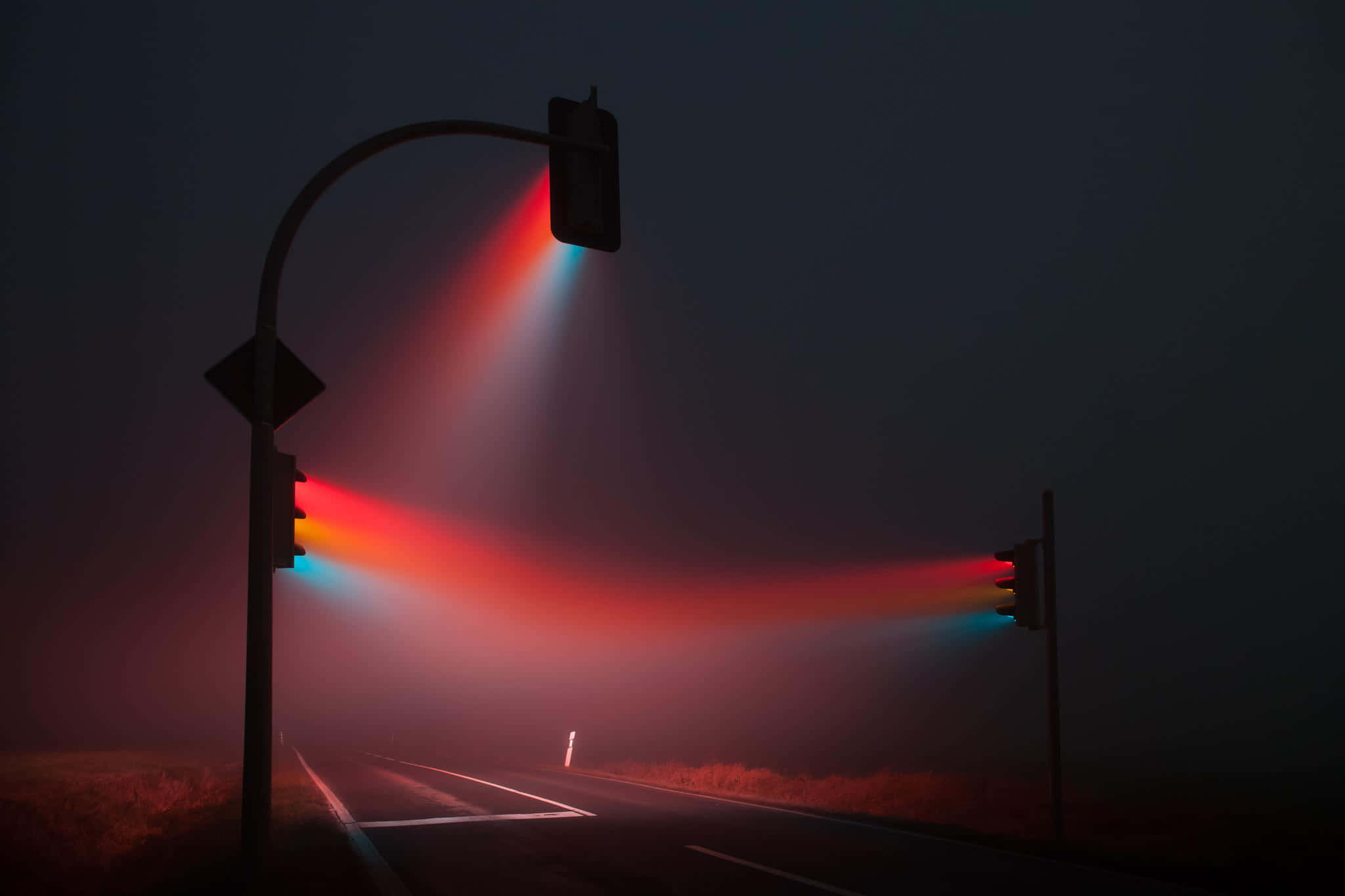 光 桌布 壁紙 — 霧氣瀰漫的夜晚道路，被發光的紅色和藍色交通燈照亮，透過霧氣投射出戲劇性的光束。