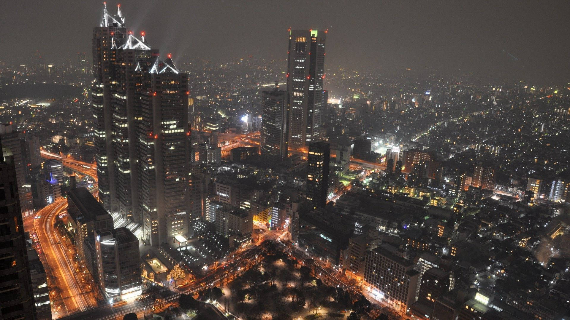 密集市區的夜間鳥瞰圖，燈火通明的摩天大樓和街道。
