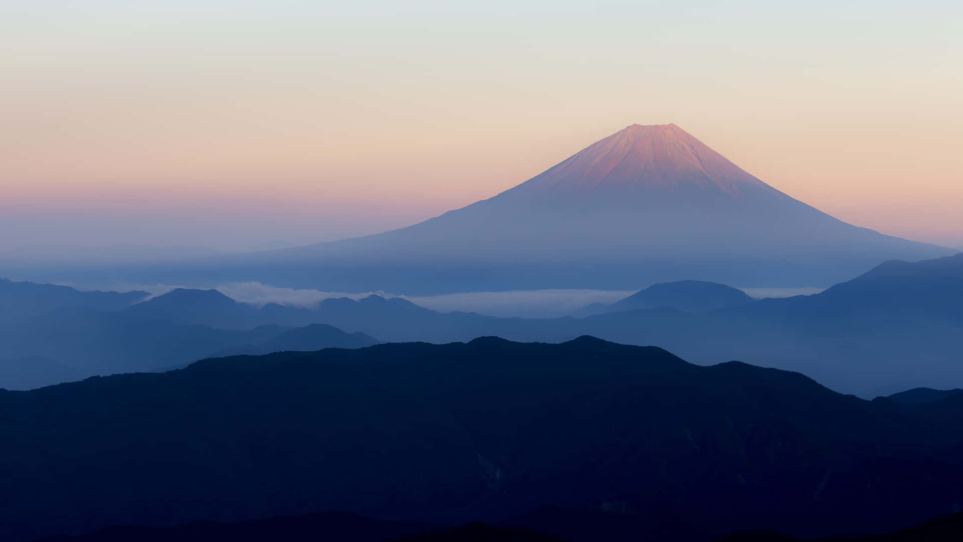 黎明時分的富士山，層疊山巒輪廓之上有粉紅色和藍色的天空。