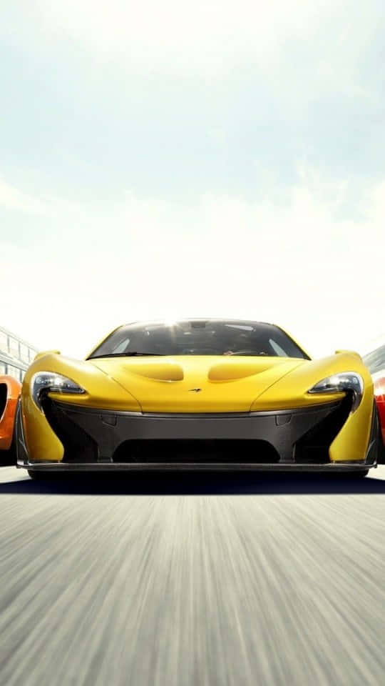 霧氣繚繞的寧靜湖畔 壁紙 — 一輛亮黃色的McLaren P1超級跑車在晴朗天空下，伴隨動態模糊效果在賽道上疾馳。