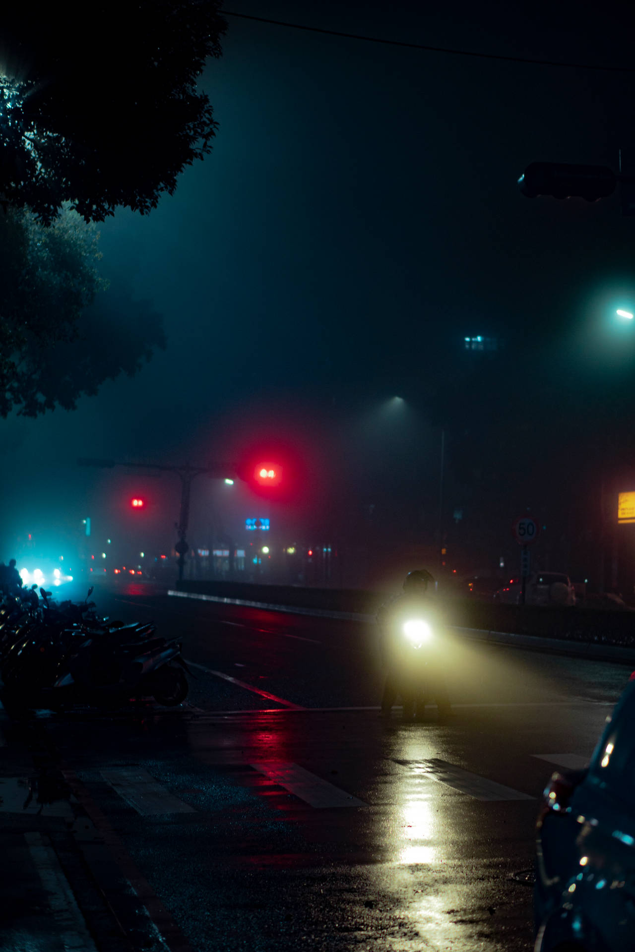 電單車手在夜間濕滑的城市街道上，紅色交通燈穿過霧氣閃爍。