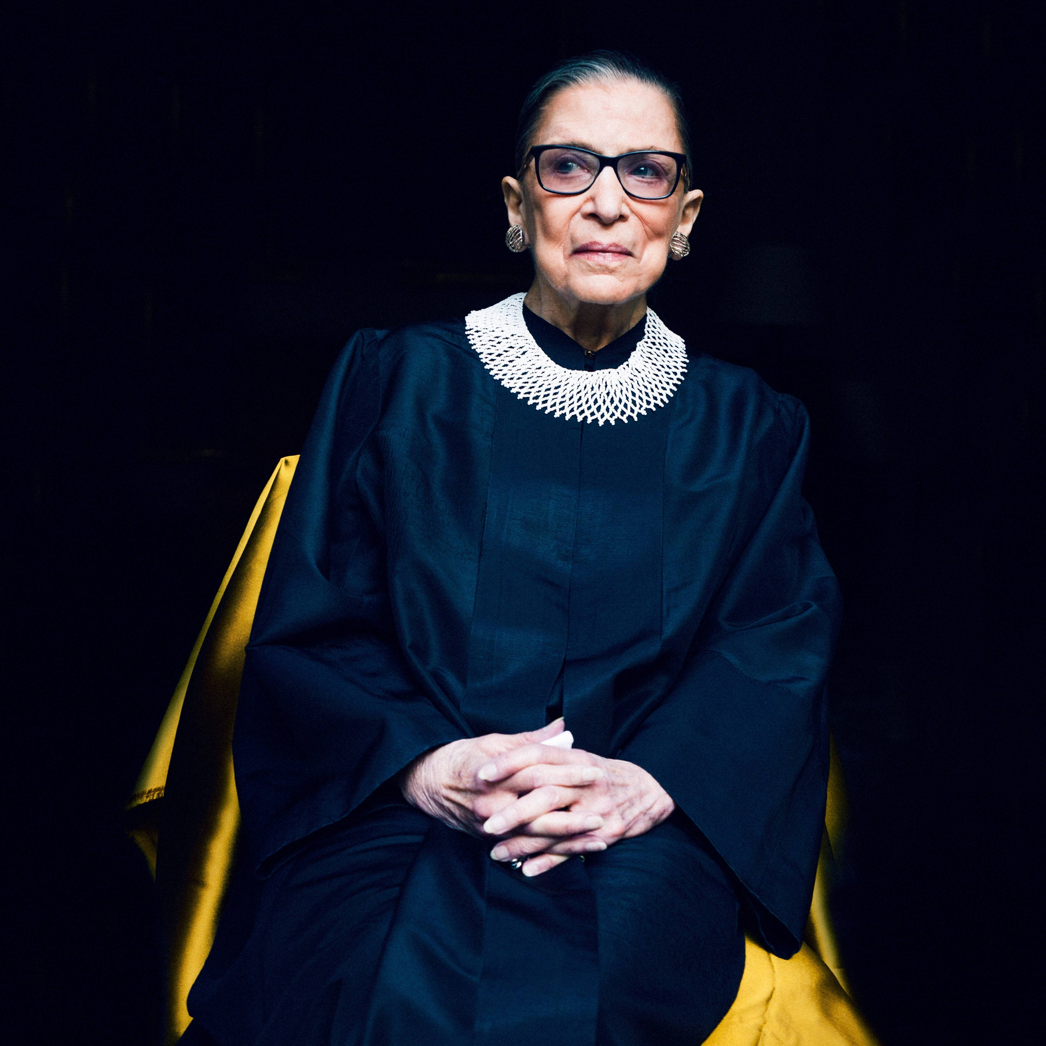 露絲·巴德·金斯伯格單色黑袍 壁紙 — 一幅莊嚴的肖像，描繪Ruth Bader Ginsburg坐在金色椅子上，身穿標誌性的黑色法官袍和白色領飾，背景為深色。