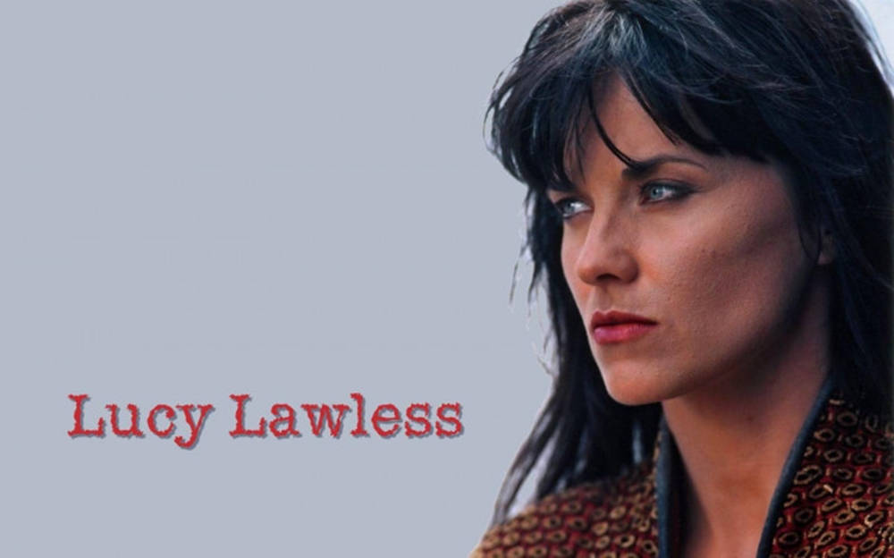 露西·勞勒斯甜美肖像照 壁紙 — 露西·勞萊斯（Lucy Lawless）在純灰色背景上，深色頭髮和紅唇，名字以紅色文字顯示，目光專注。