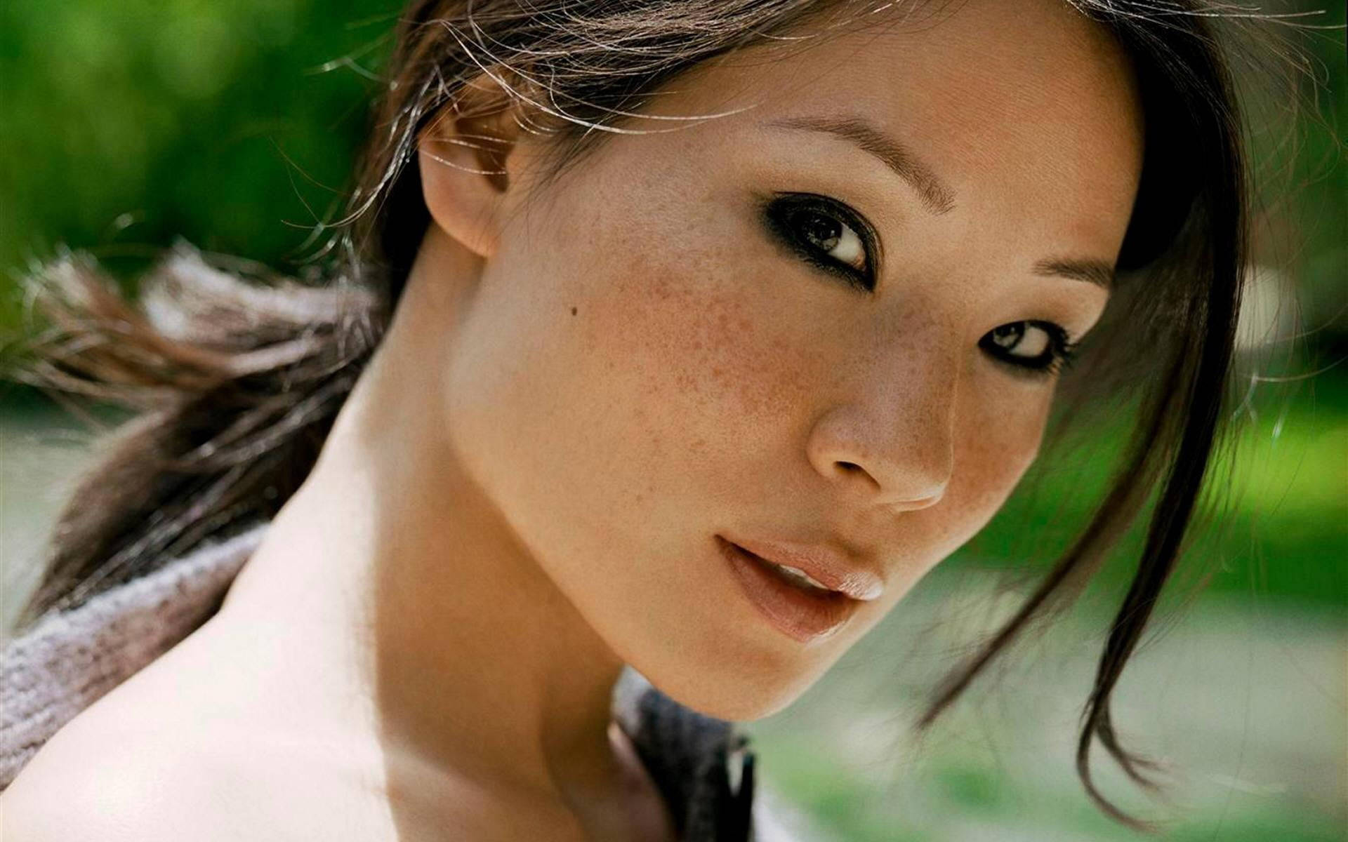 露西·李性感風采 壁紙 — 一個特寫肖像，一位擁有深色眼睛和雀斑的女性，在模糊的綠色背景下直視鏡頭。