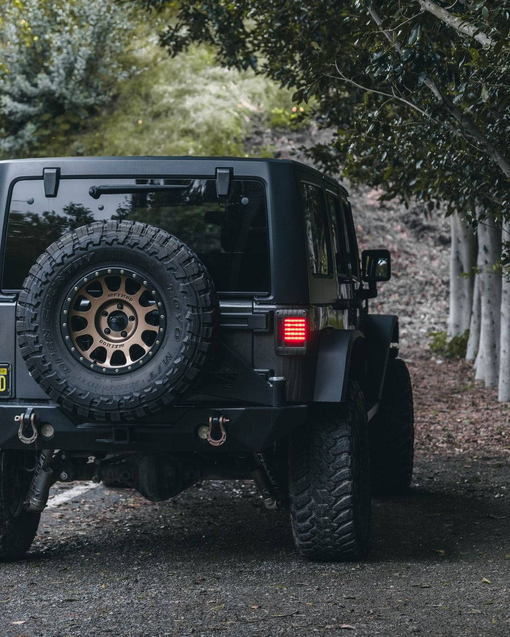 黑色Jeep Wrangler在森林中的碎石路上行駛。