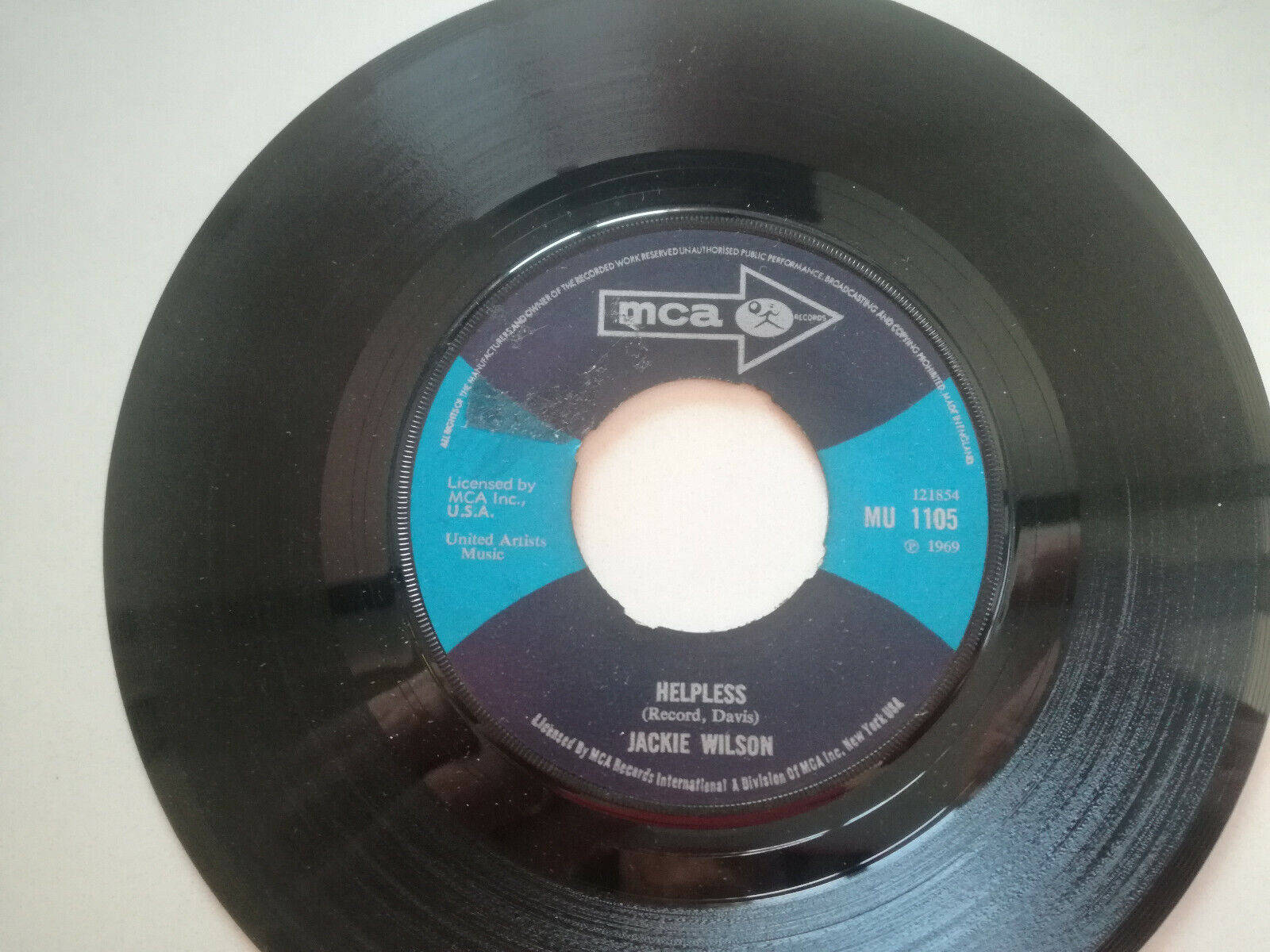 靈魂樂傳奇Jackie Wilson手持黑膠唱片 壁紙 — MCA唱片公司Jackie Wilson歌曲《Helpless》的復古黑色黑膠唱片標籤特寫，採用藍黑設計。