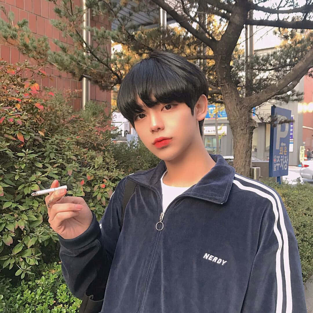 青春在日常時光中的歡愉 壁紙 — 一位黑髮紅唇的年輕男子，身穿帶有白色條紋的海軍藍天鵝絨外套，在戶外拿著一支香煙。