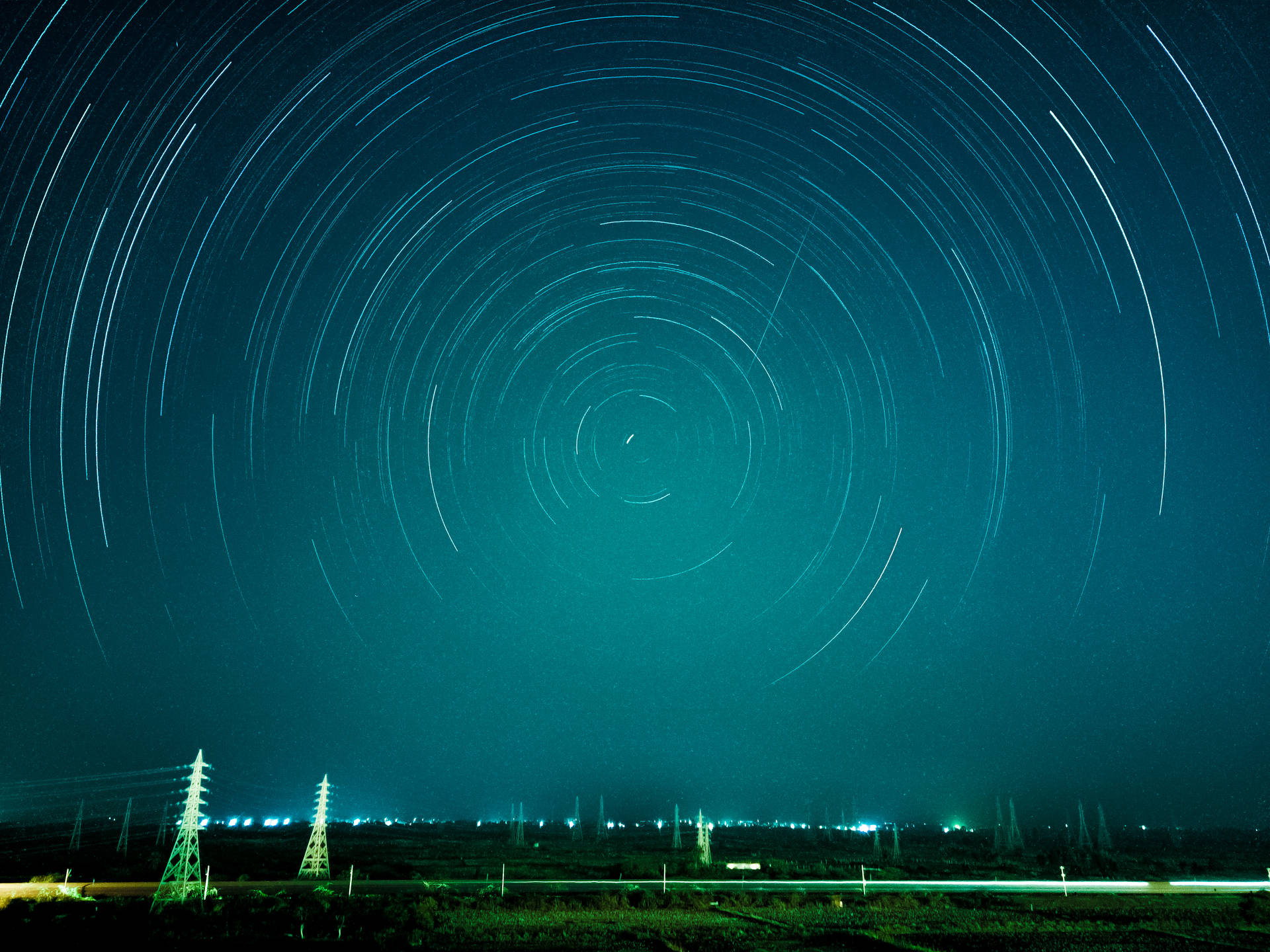 星軌在青綠色夜空下，在電線和城市燈光之上旋轉。