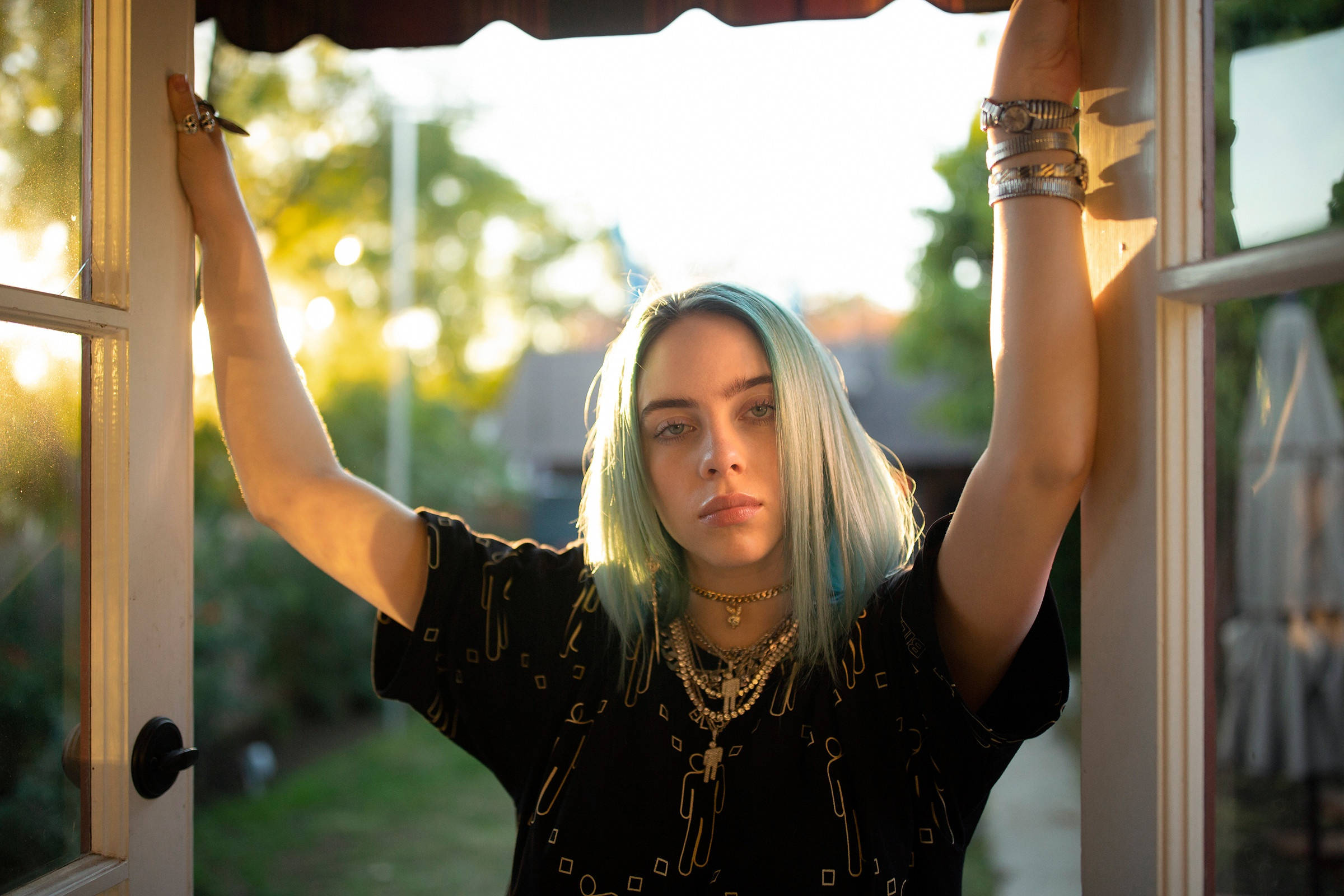 青綠挑染髮型比莉·艾利什 4K 壁紙 — Billie Eilish 舉起雙臂，靠喺陽光普照嘅窗框上，佢嘅藍色頭髮喺金色午後光線中閃耀。