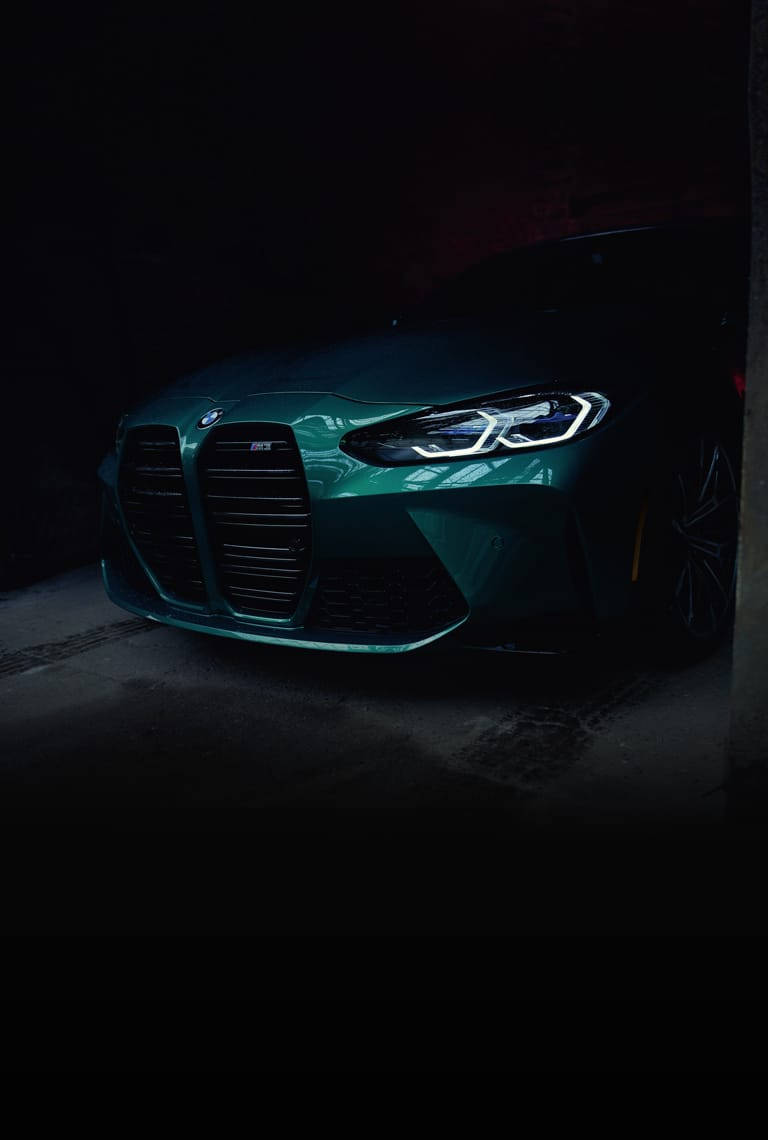 青綠色BMW M3在光線昏暗的車庫中，帶有發光的車頭燈和時尚的設計。