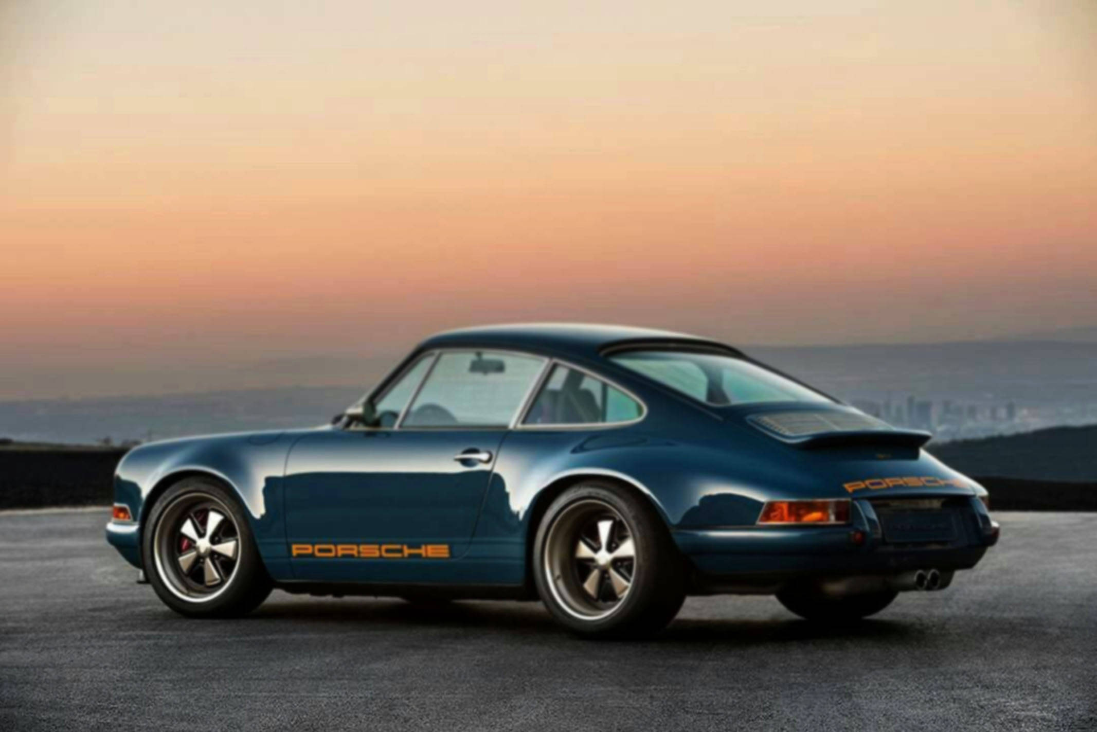 青綠色Singer Porsche黃昏灣畔 壁紙 — 一架時尚的藍色保時捷911經典跑車停泊在山頂上，夕陽西下，遠處是城市景觀。