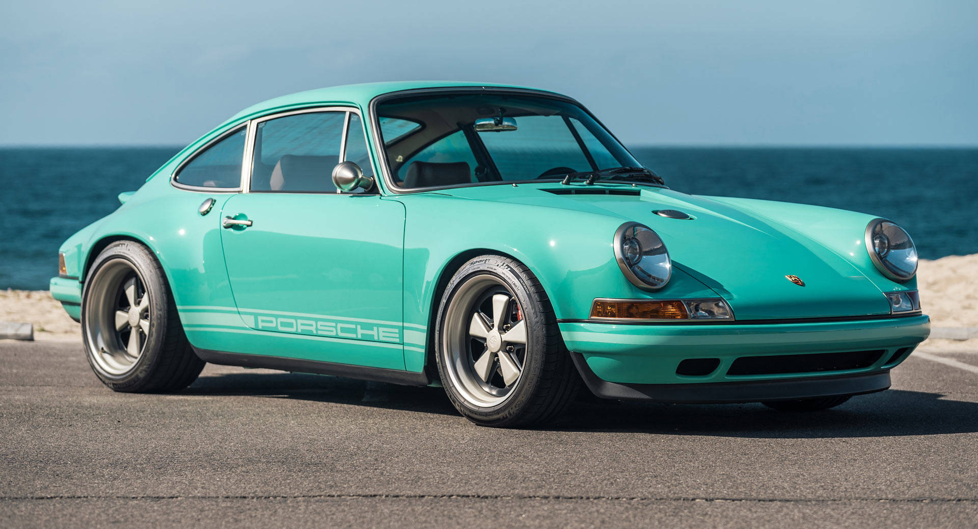 青綠色Singer保時捷911 壁紙 — 一輛充滿活力的青綠色保時捷911經典跑車停泊在沿海公路上，背景是海洋。
