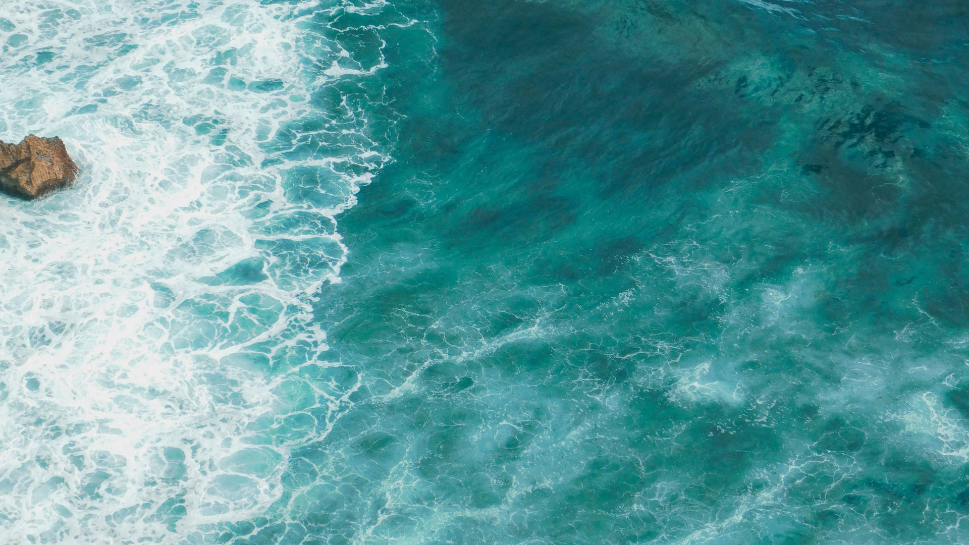 青綠色海洋波浪 壁紙 — 從高空俯瞰，碧綠色的海浪拍打岩石露頭，激起白色泡沫。