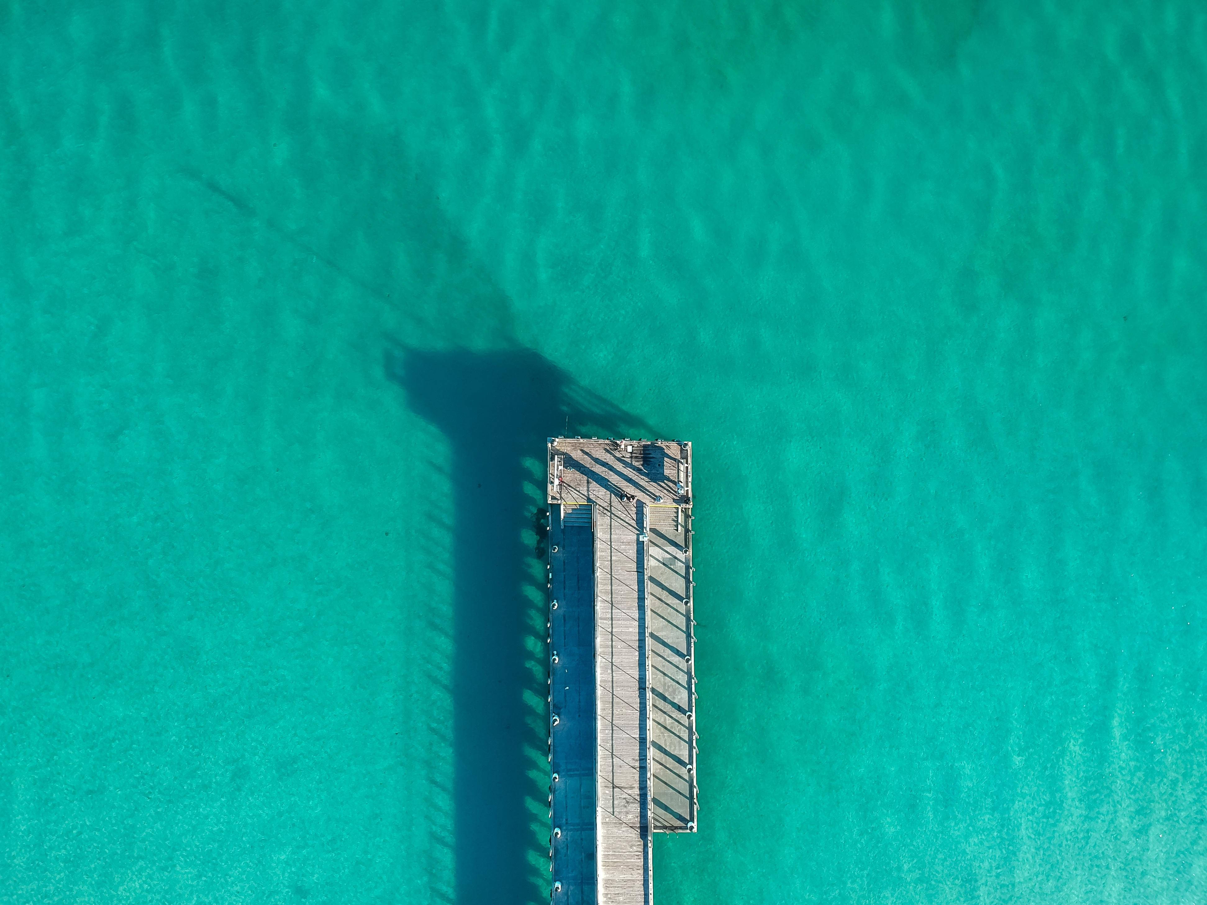 青綠色海洋碼頭 壁紙 — 木製碼頭的鳥瞰圖，在充滿活力的碧綠海水中投下長長的陰影。