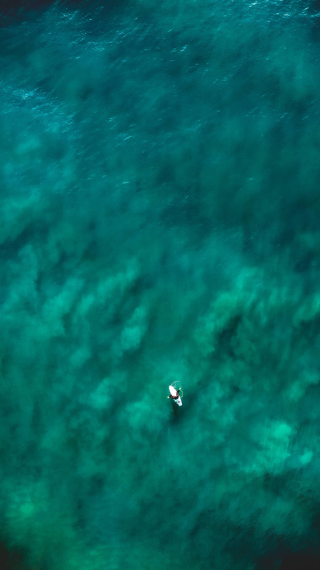 一名衝浪者從上方在清澈碧綠的海水中衝浪。