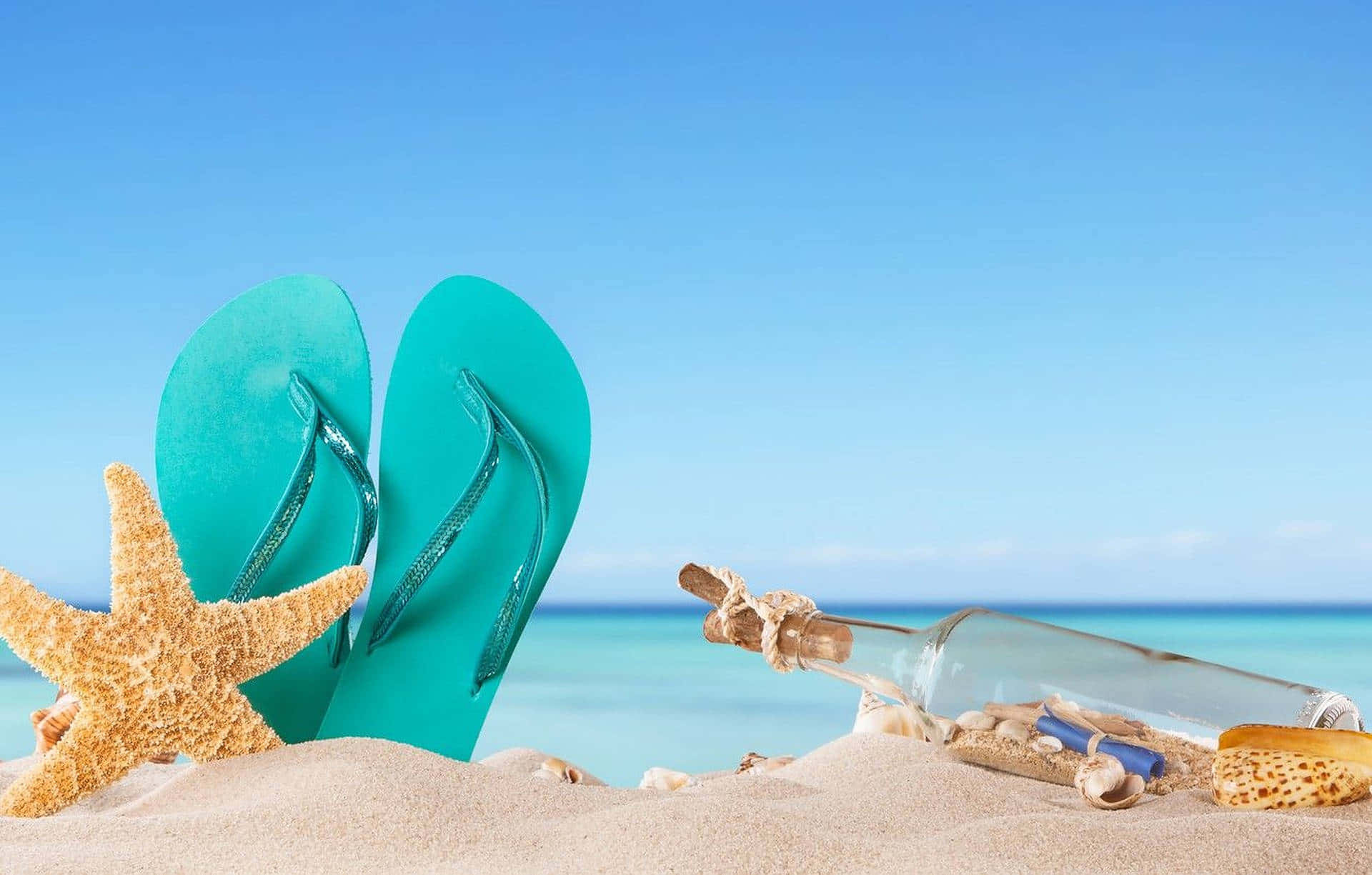 Beach Getaway 桌布 壁紙 — 青綠色的拖鞋和海星放在陽光普照的沙灘上，旁邊有一個裝著訊息的瓶子，靠近海洋。