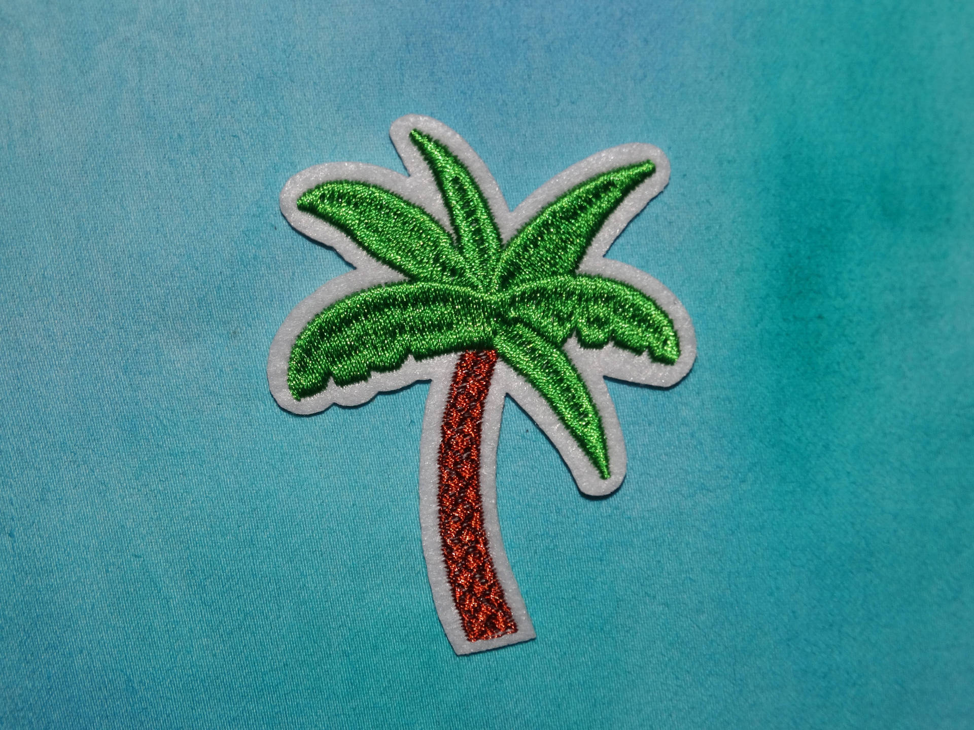 青綠色布料上帶有閃亮樹幹的刺繡棕櫚樹補丁。