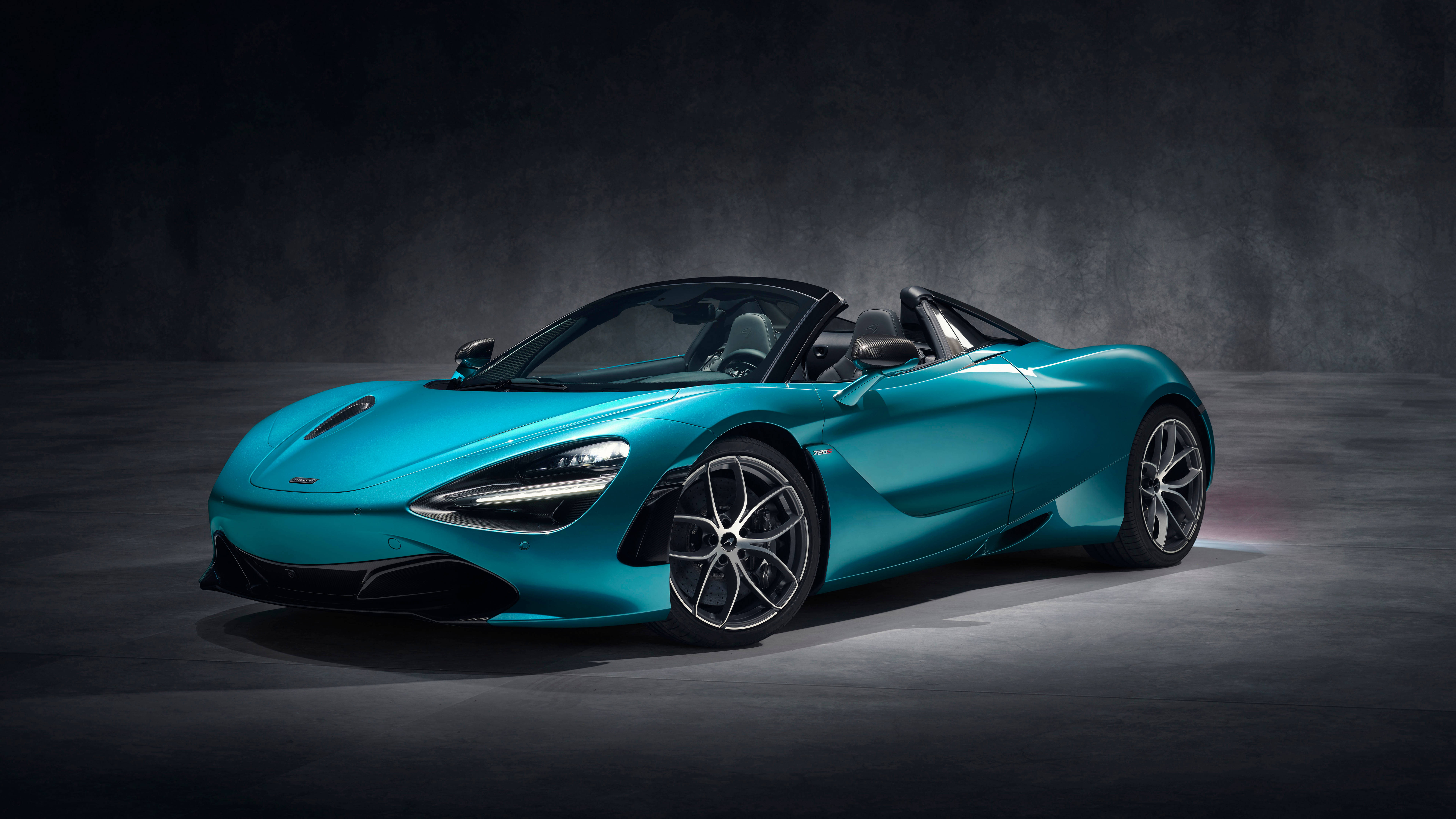 青綠色麥拉倫720S 壁紙 — 一輛時尚的藍綠色McLaren 720S Spider開篷跑車在攝影棚燈光下，於深色紋理背景前閃閃發光。