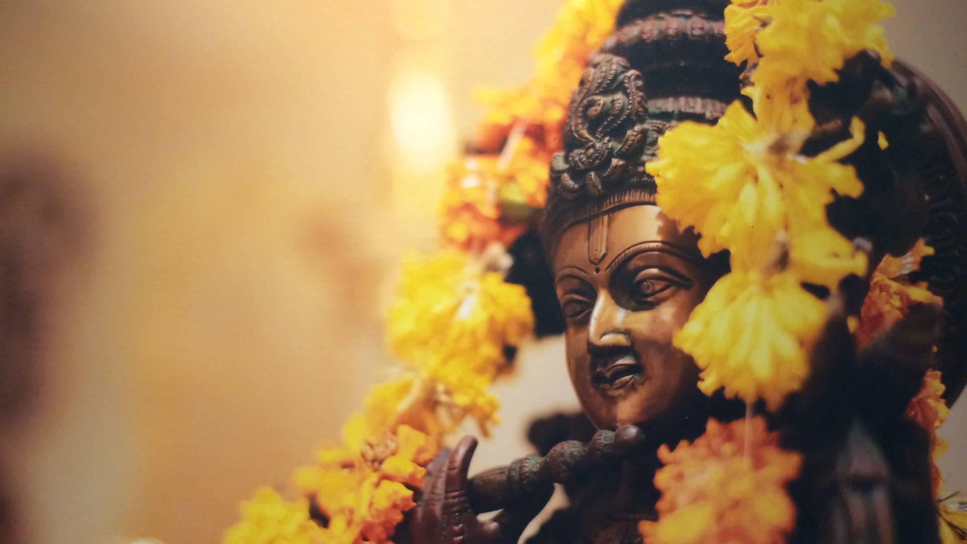 Krishna HD 桌布 壁紙 — 青銅神像特寫，飾以鮮黃色萬壽菊，背景溫暖模糊。