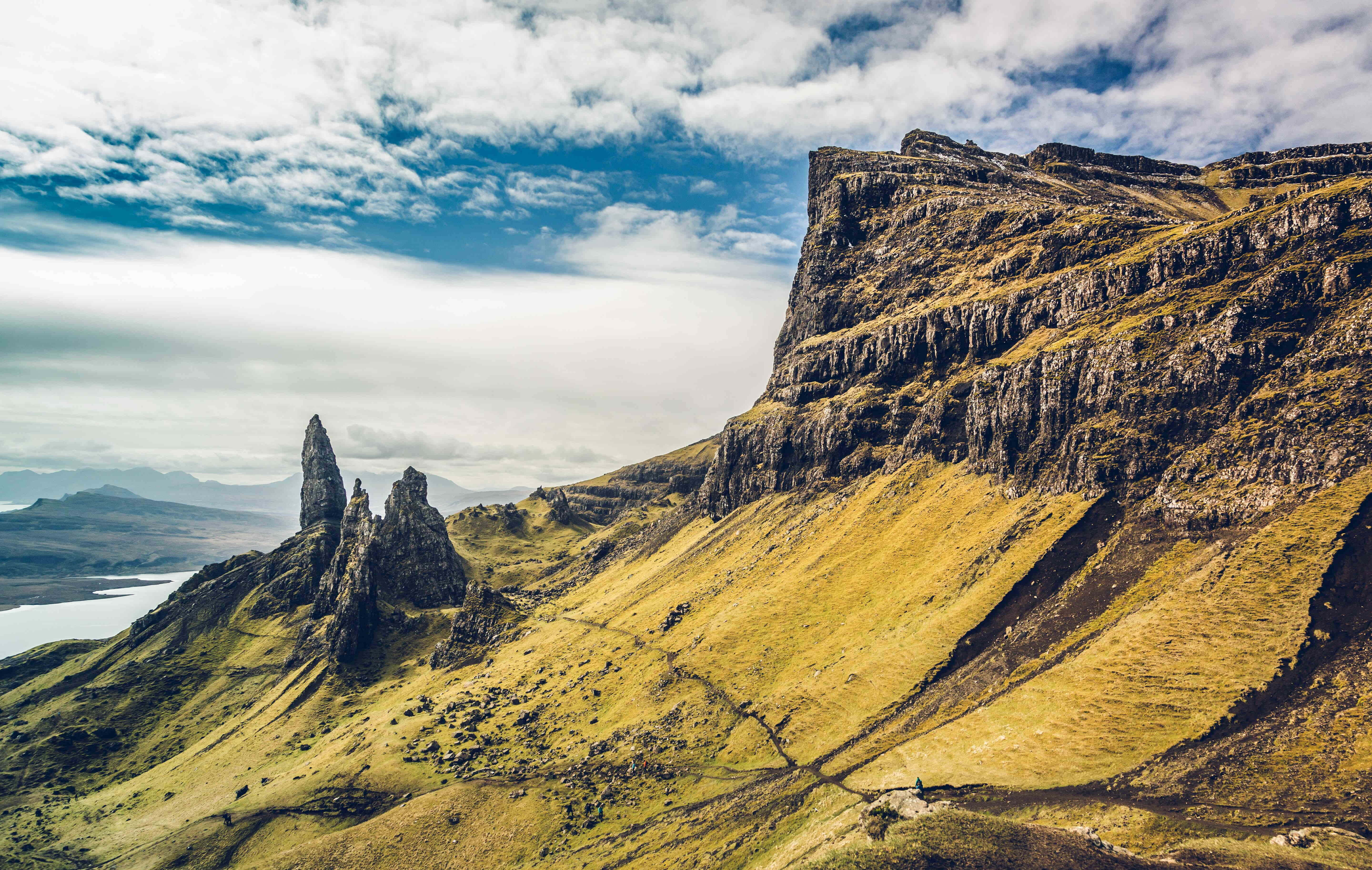 靜心欣賞大自然的純粹之美 壁紙 — 崎嶇的山峰和草坡，在戲劇性的多雲天空下，遠處有湖泊和山丘。