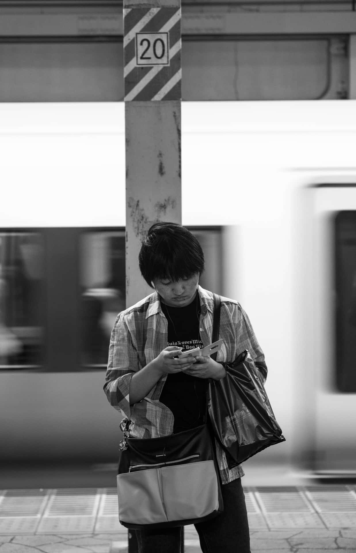 人在火車站月台上等候，看著手機，火車駛過。