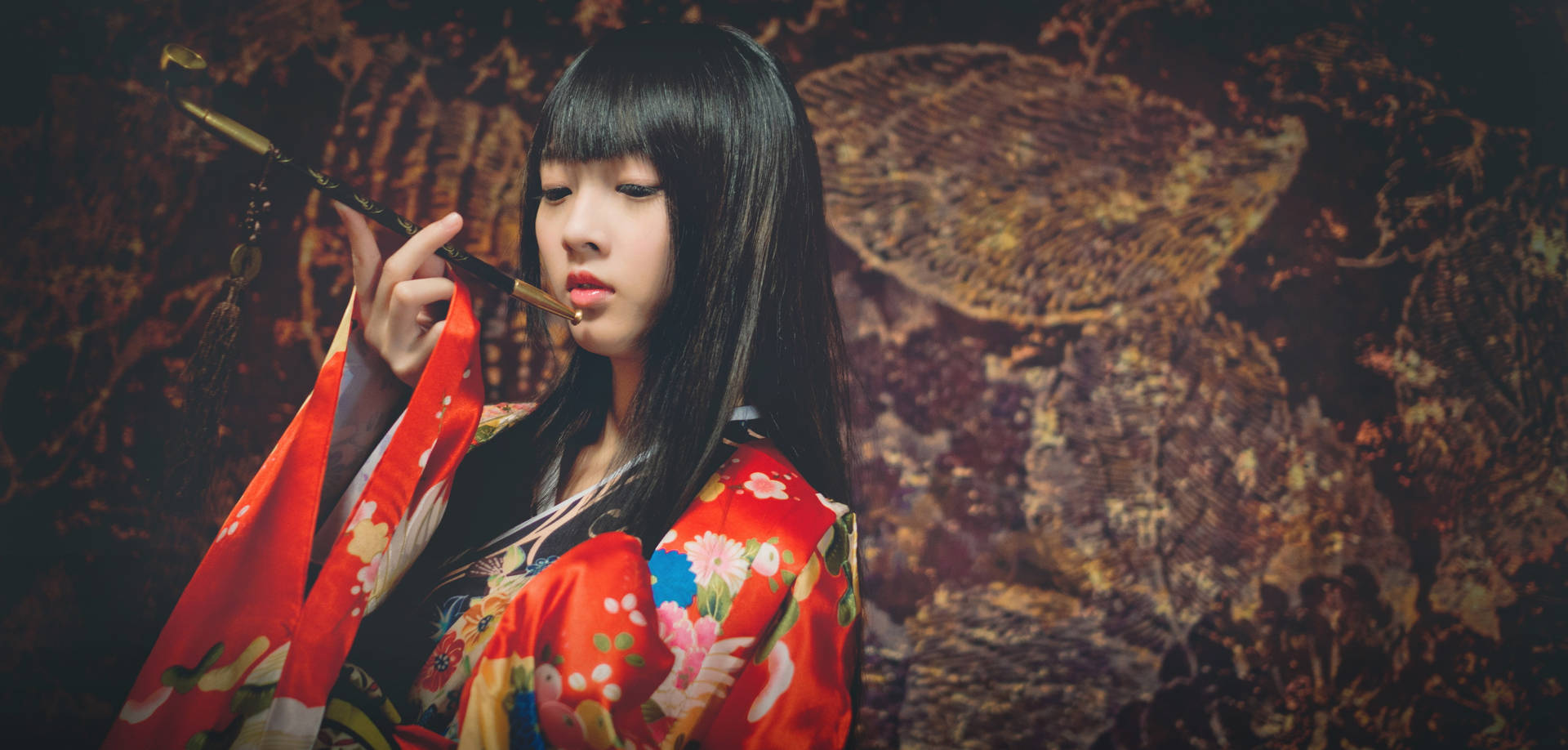 身穿紅色花卉和服的女子，在深色質感背景前手持煙斗。