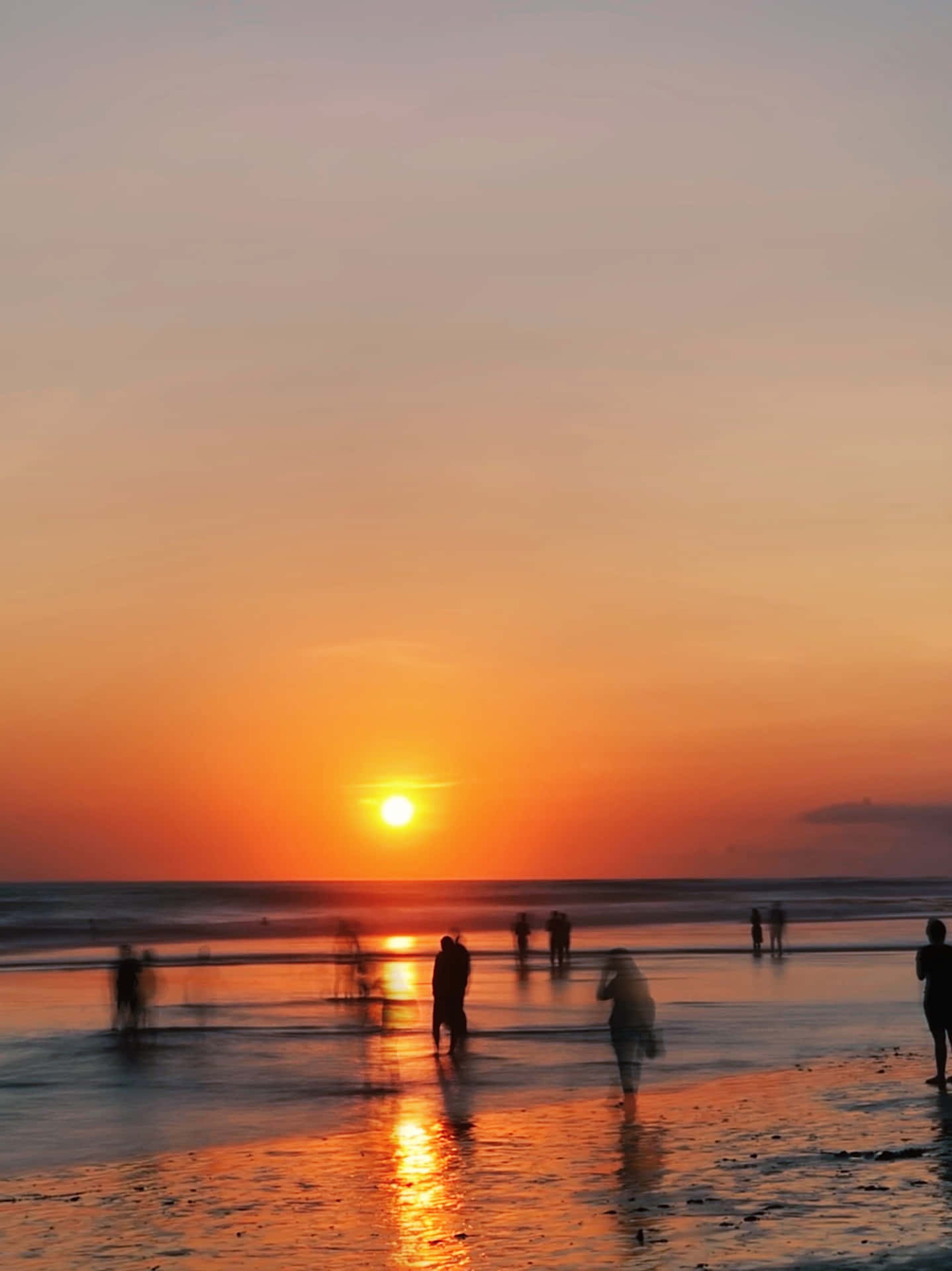 人們在濕沙灘上行走，橙色夕陽映照海洋