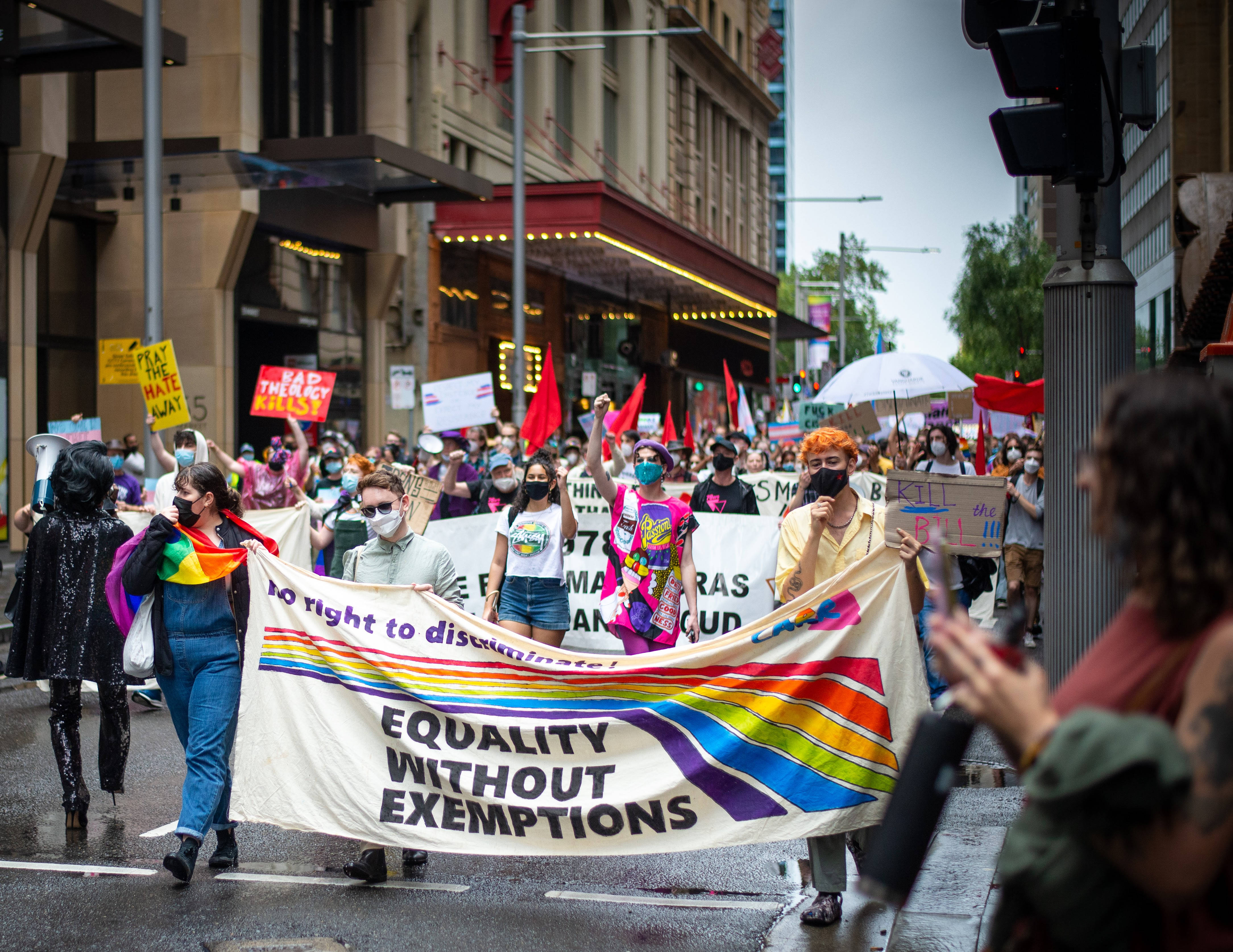 非二元人士為無差別平等抗議 壁紙 — 一場充滿活力的LGBTQ+驕傲遊行擠滿了濕漉漉的城市街道，參與者高舉彩虹橫幅和標語，要求平等，不設例外。