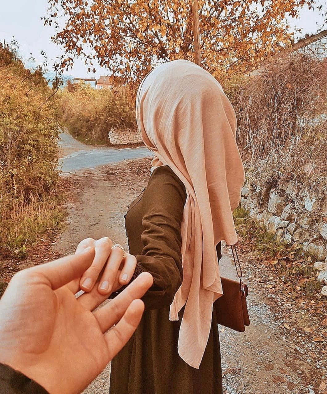 手牽著一位身穿米色頭巾的女子走在秋日小徑上。