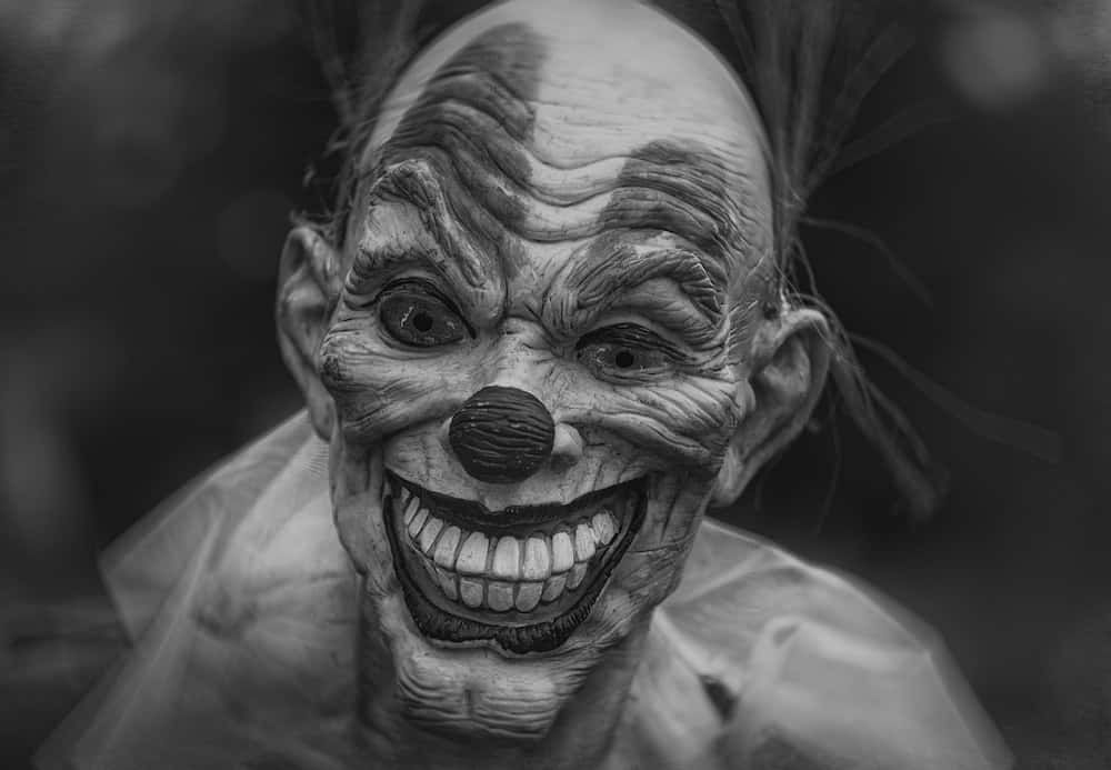 面帶微笑的小丑 壁紙 — 一個可怕詳細的黑白特寫，一個怪誕的小丑，有著深深的皺紋和寬闊的露齒笑容。