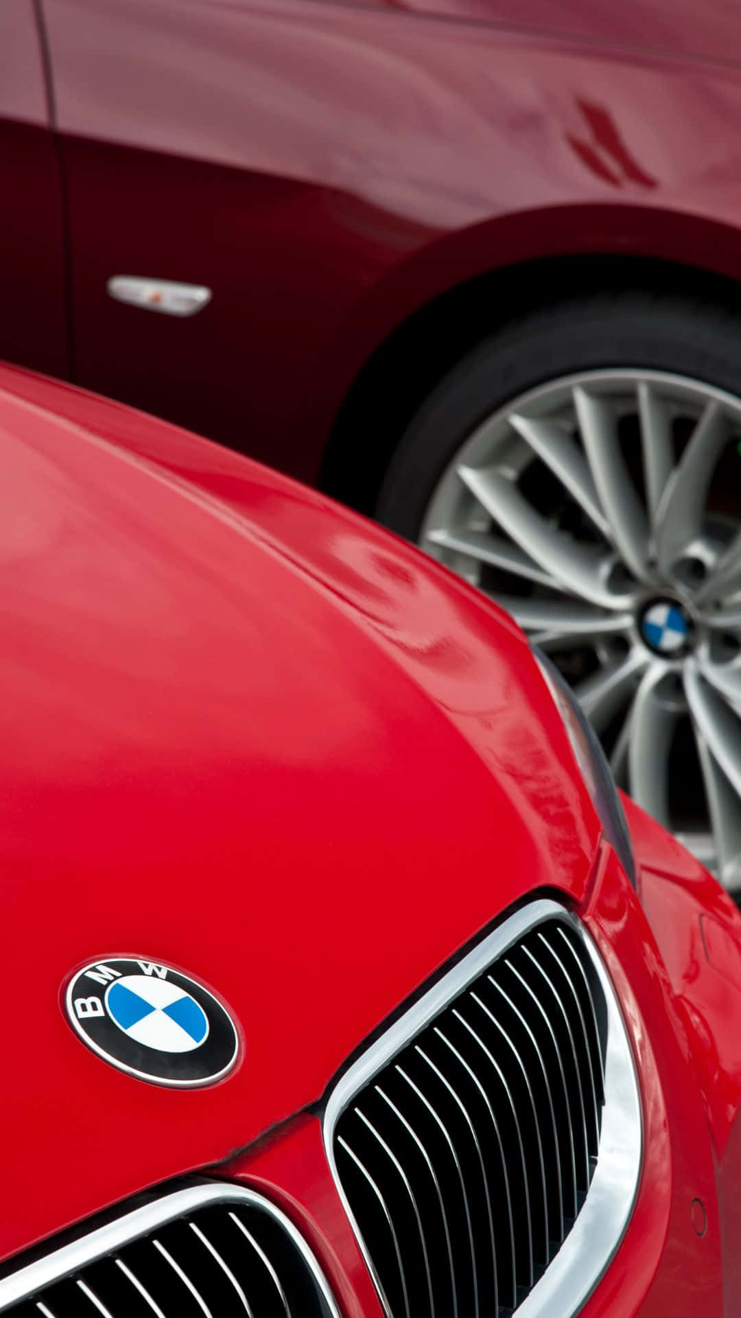 革新駕駛體驗：BMW安卓相容性更新 壁紙 — 光澤紅色寶馬車頭蓋和鬼面罩的特寫，背景有一輛栗色寶馬。