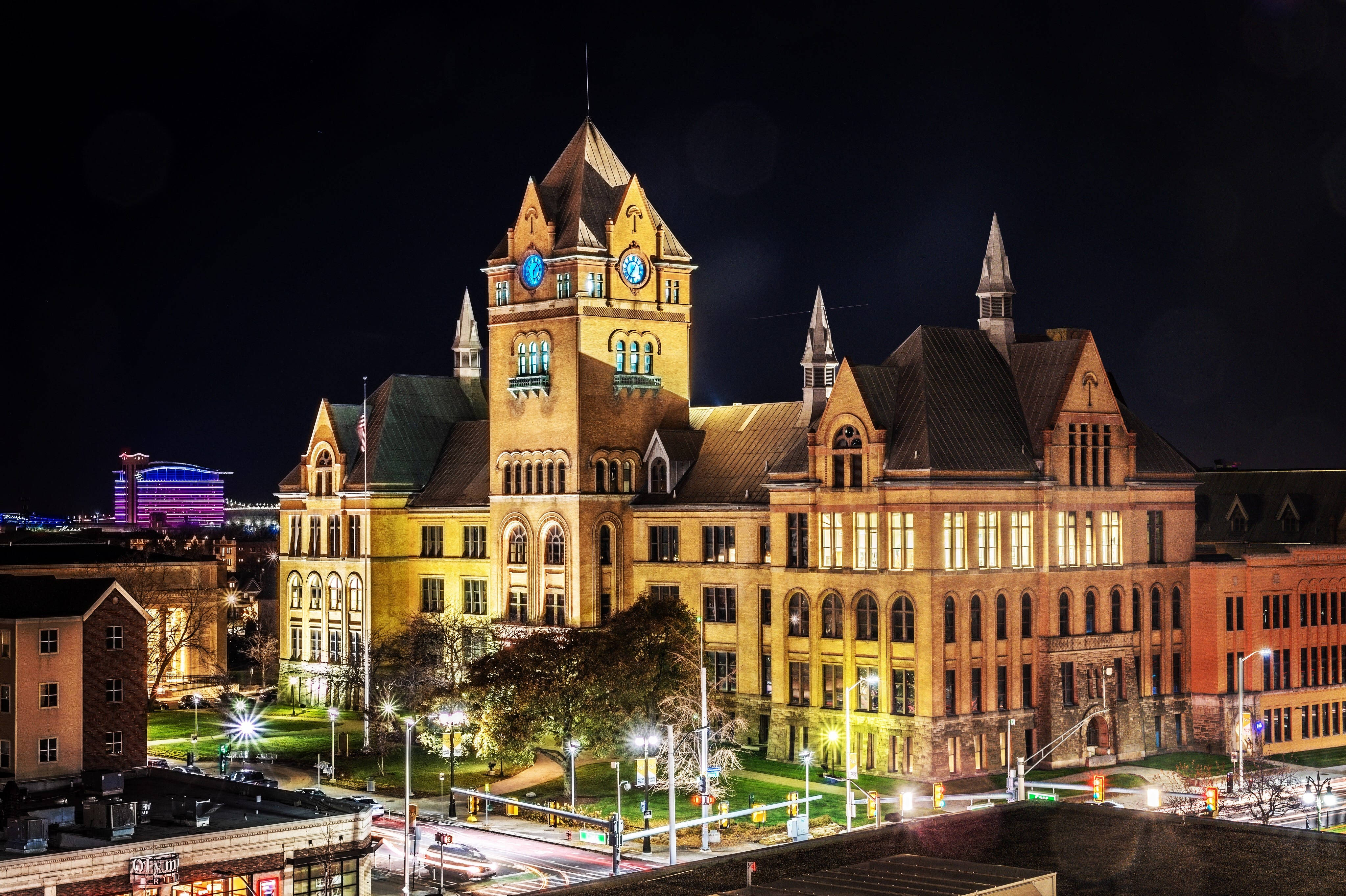 韋恩州立大學舊主樓夜景 壁紙 — 一座宏偉的歷史法院在夜晚被溫暖的燈光照亮，背景是黑暗的天空和遠處的城市燈光。