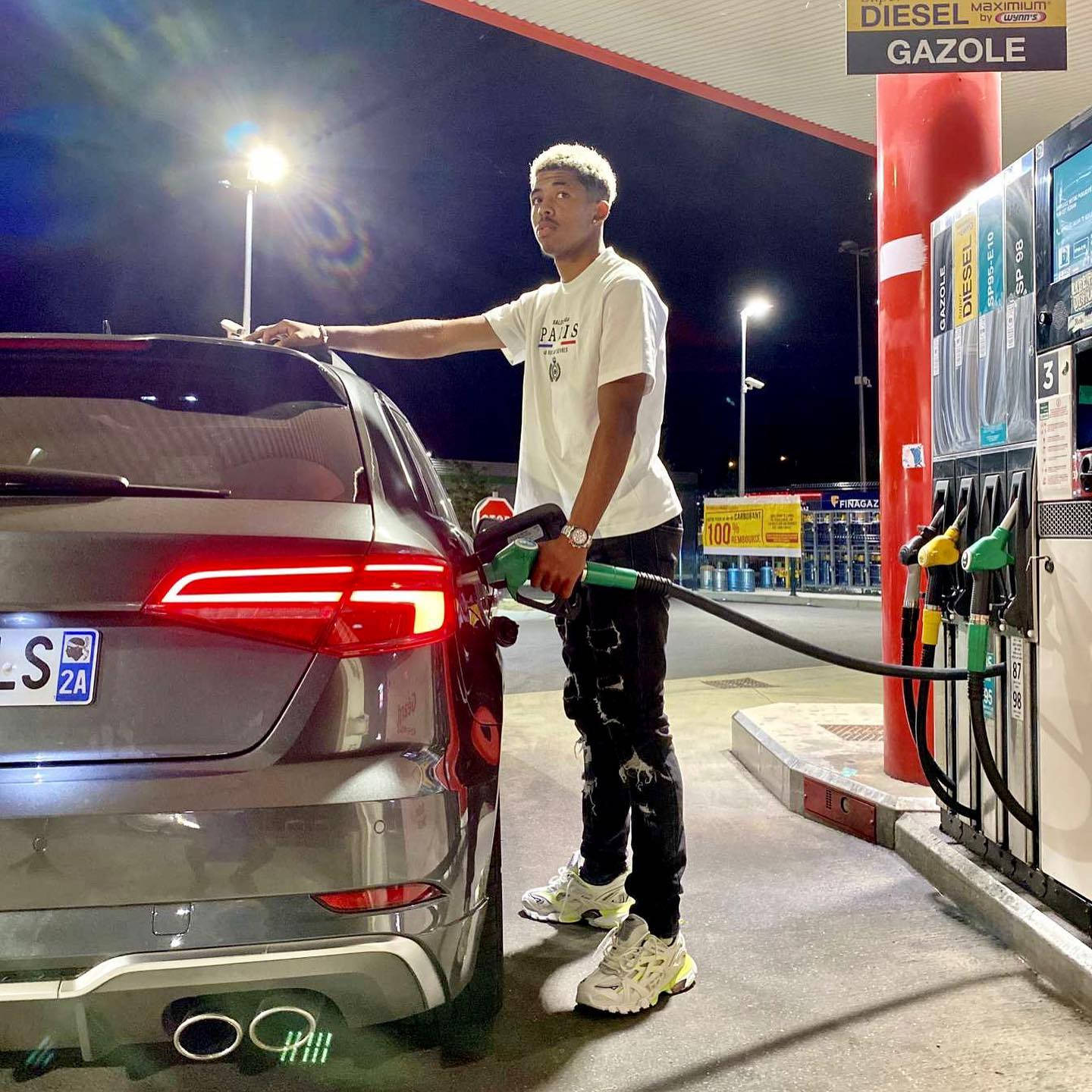 韋斯利·福法納加油站 壁紙 — 一名年輕男子在夜晚明亮的加油站燈光下為銀色SUV加注柴油。
