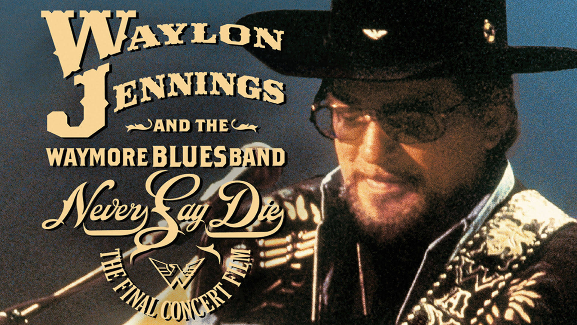 韋蘭·金尼恩斯《永不言棄》 壁紙 — Waylon Jennings 戴著黑色牛仔帽和眼鏡，在藍色背景上金色文字前微笑著拿著結他。