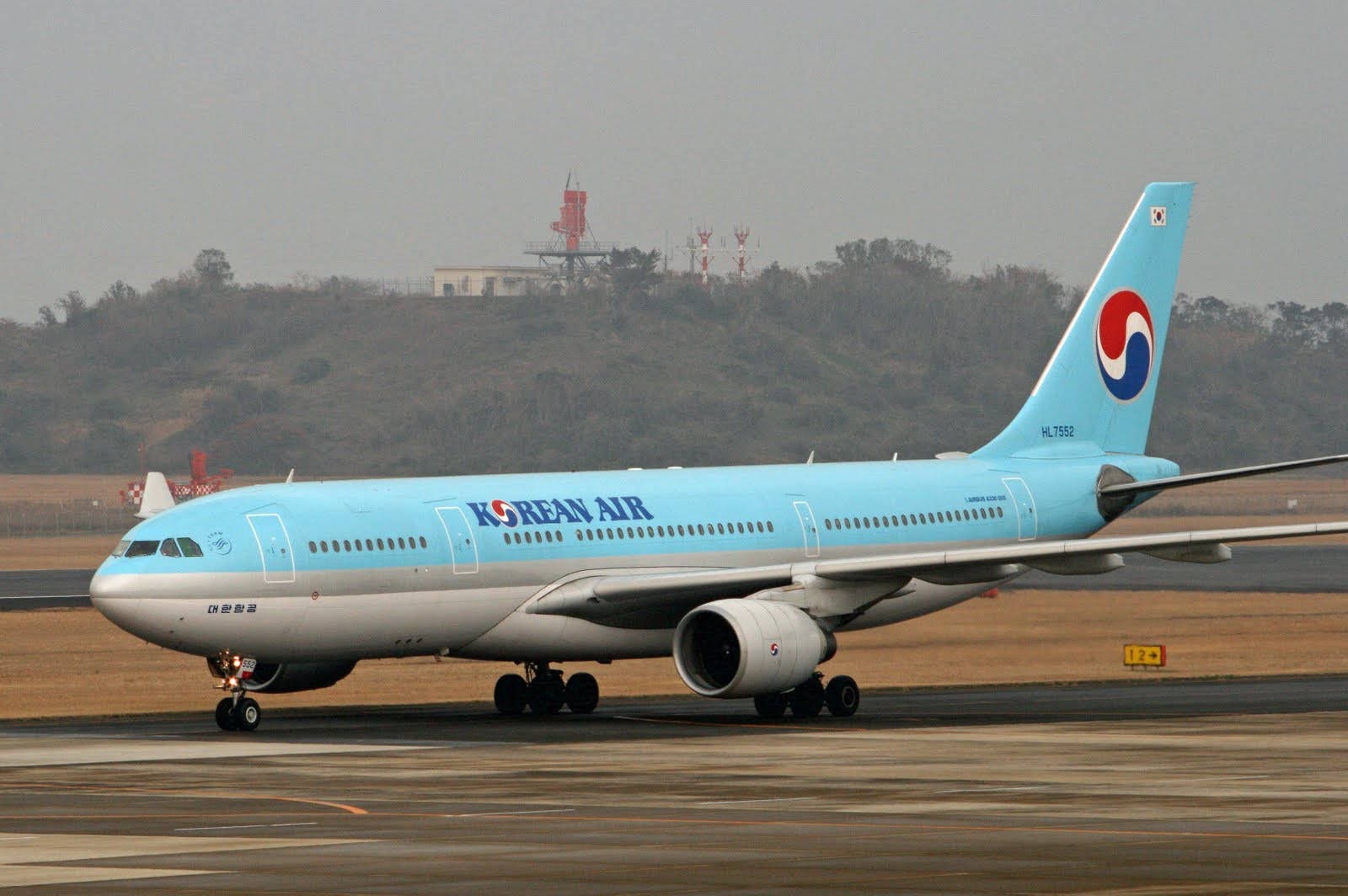 大韓航空飛機在機場跑道上，背景有朦朧山丘。