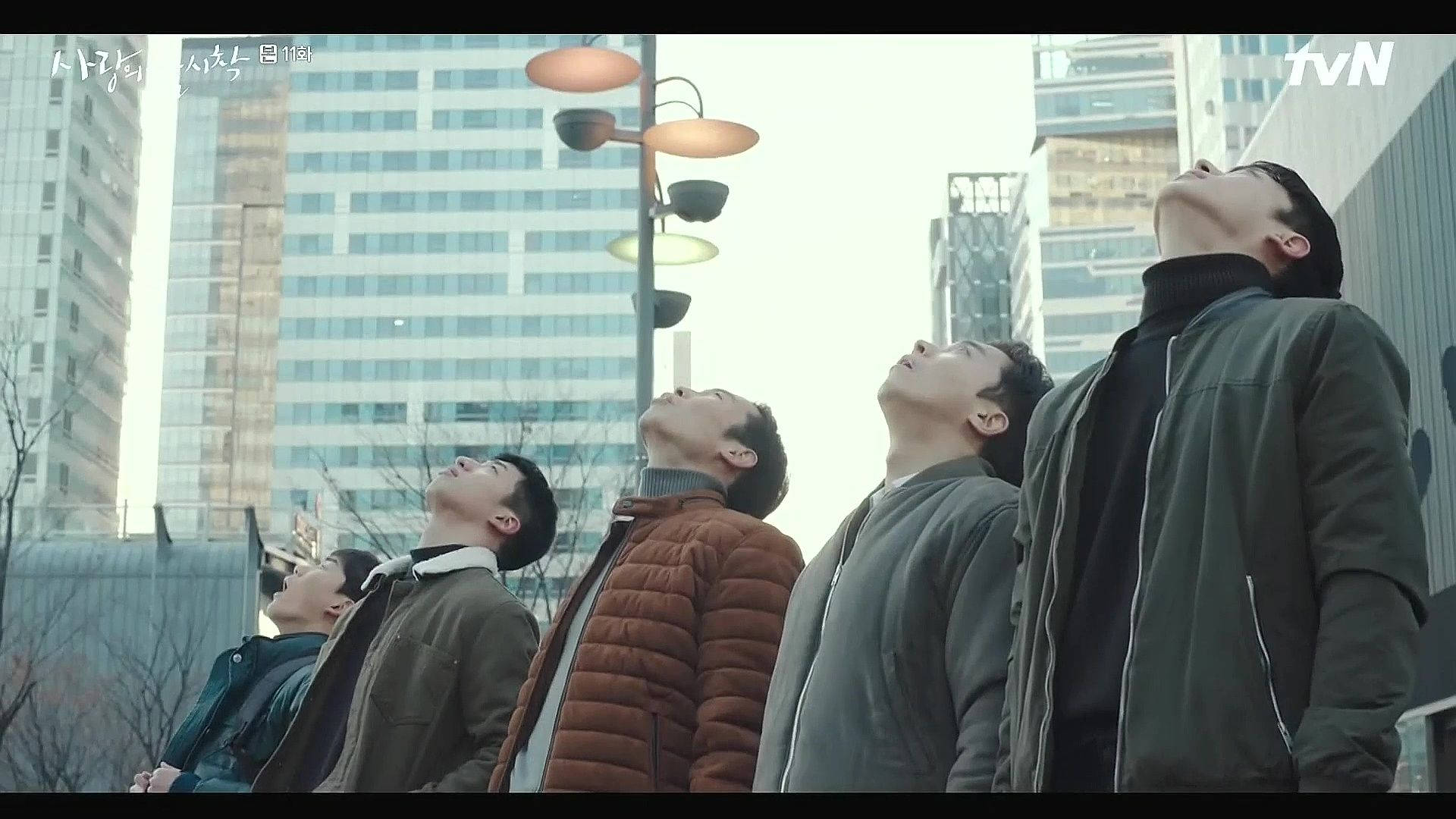 四個穿著冬季外套的男人在多雲的日子裡仰望城市建築。