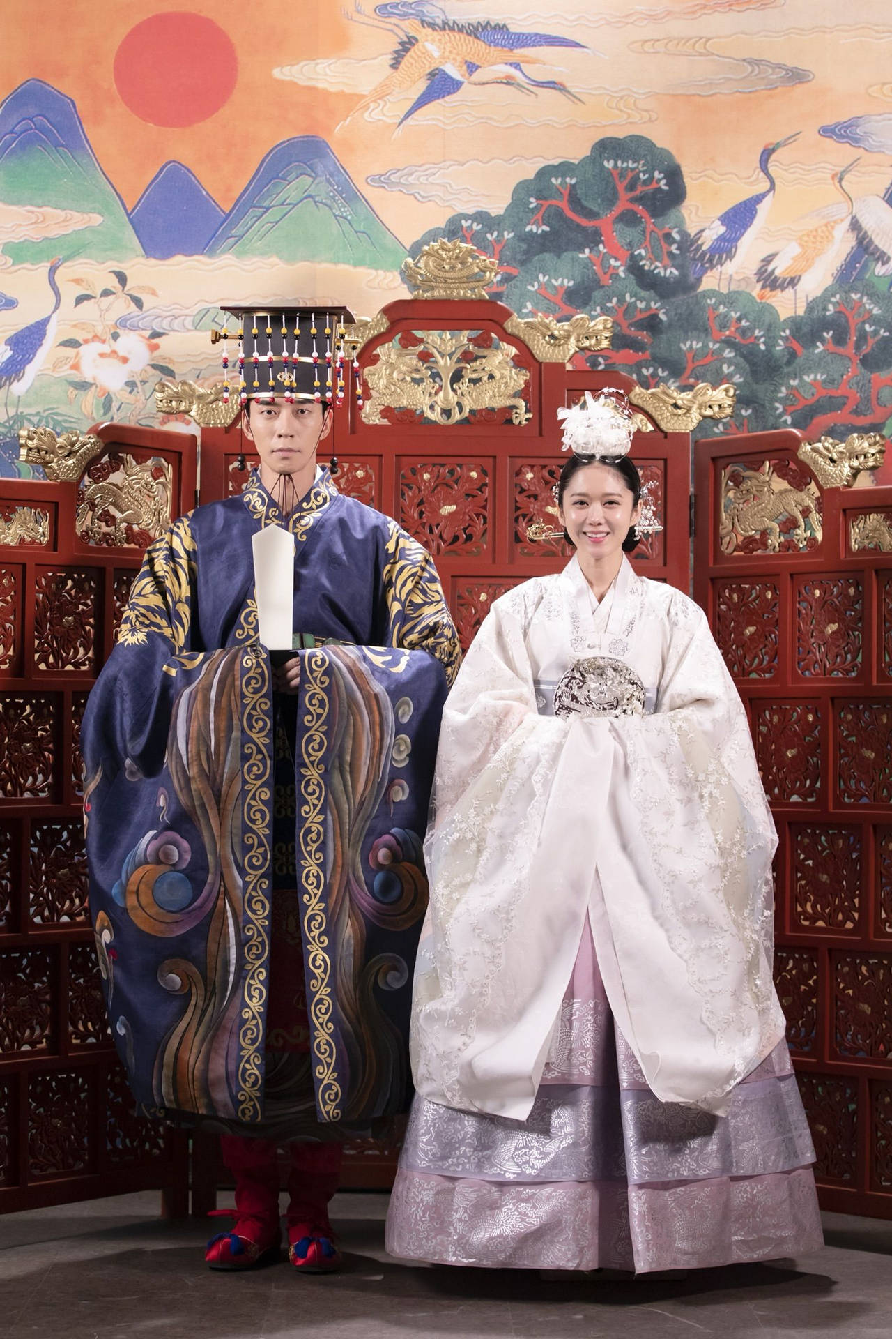 一對韓國新人穿著傳統婚禮韓服，在繪畫屏風前擺姿勢。
