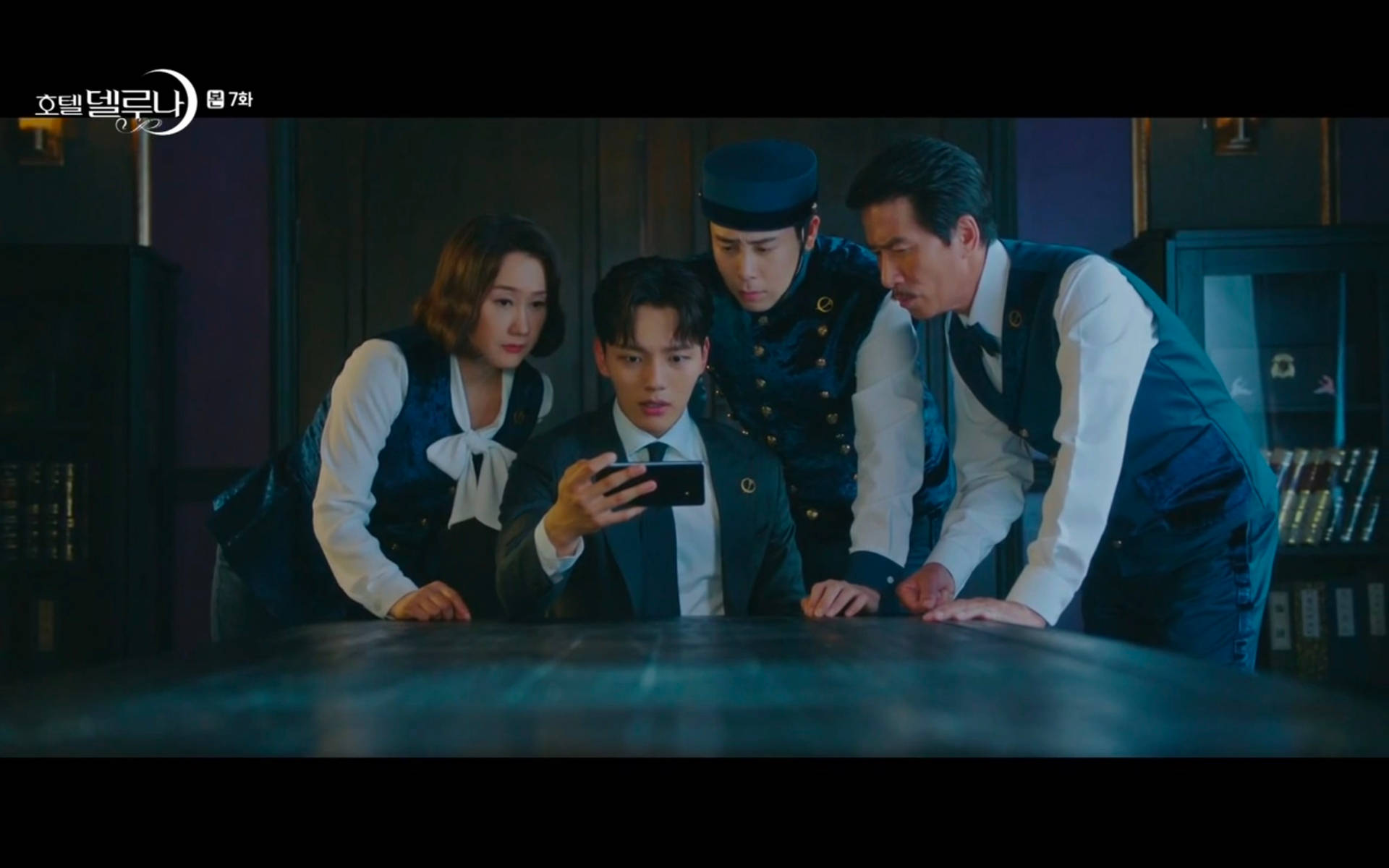 四名穿著復古制服的員工圍在桌子旁看著一部電話。