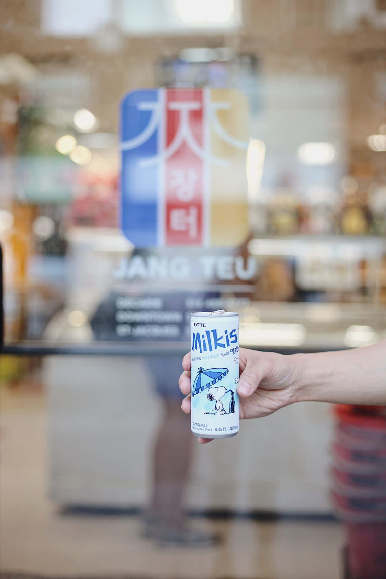 手拿著一罐Lotte Milkis，罐上有史努比在雨傘下，在商店內。
